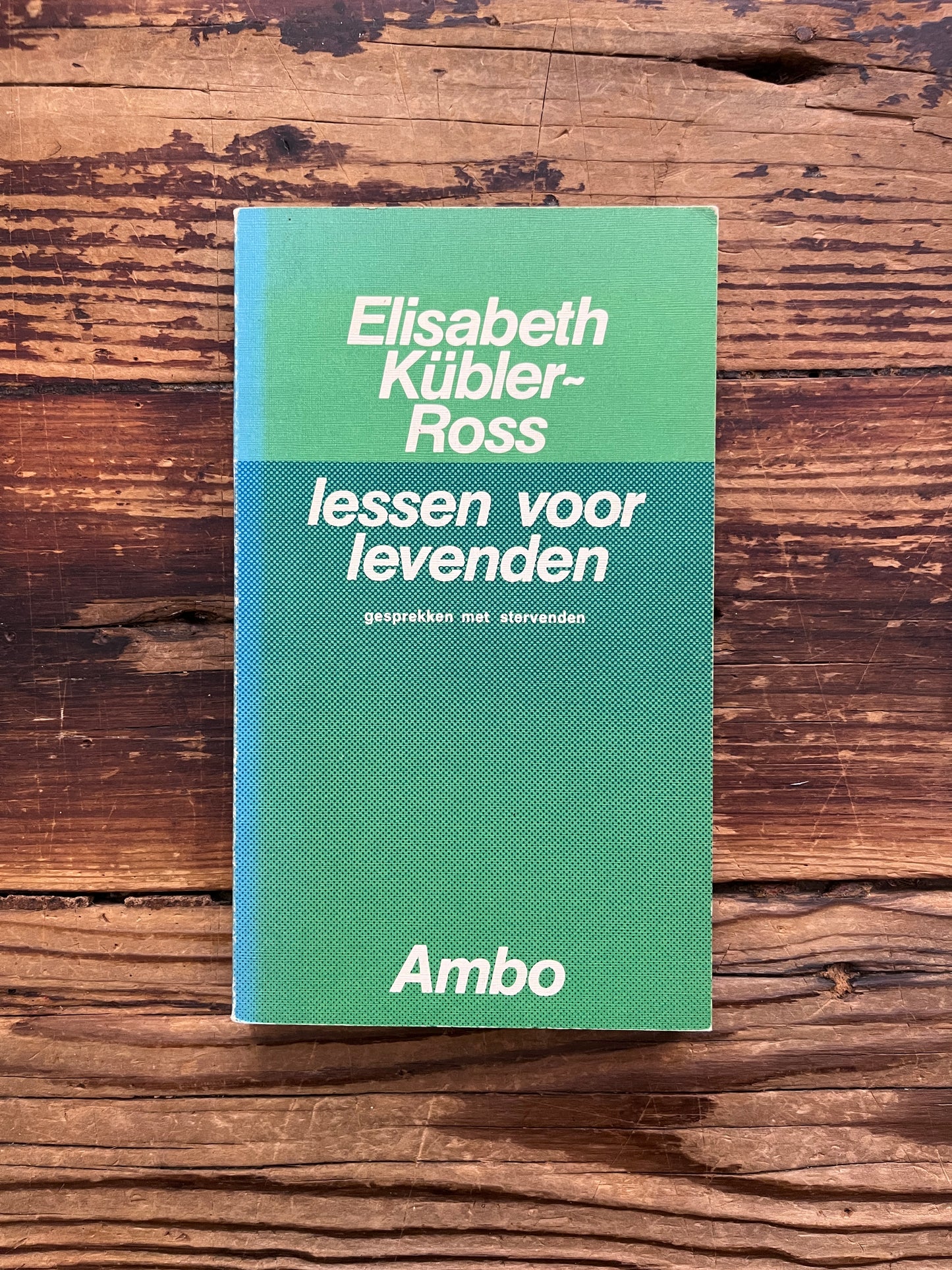 Voorkant van boek met de titel 'lessen voor levenden' door Elisabeth Kübler-Ross   op een houten achtergrond 