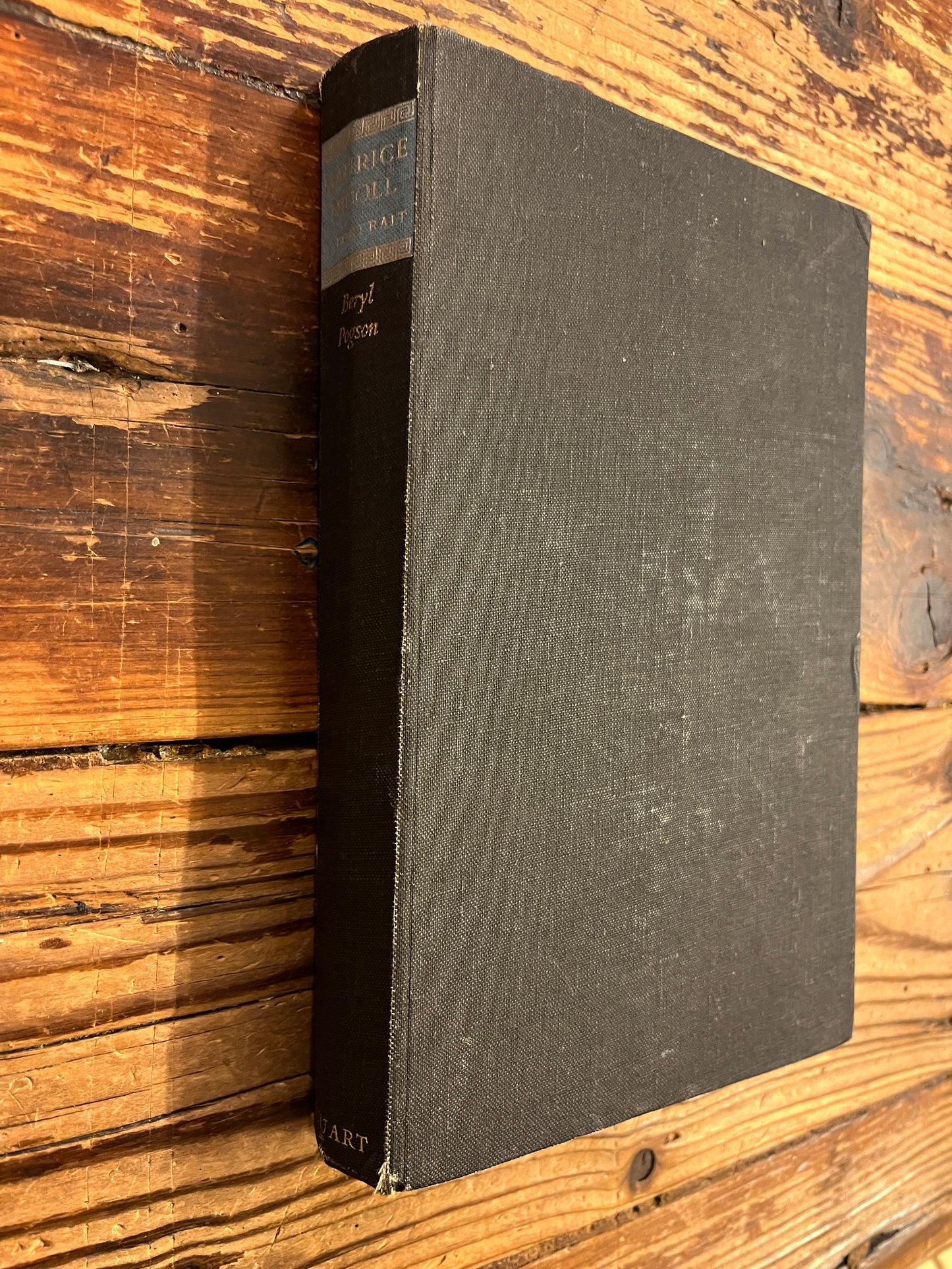 Black cloth covers and spine of book titled 'Maurcie Nicoll a portrait' by Beryl Pogson on a wooden surface