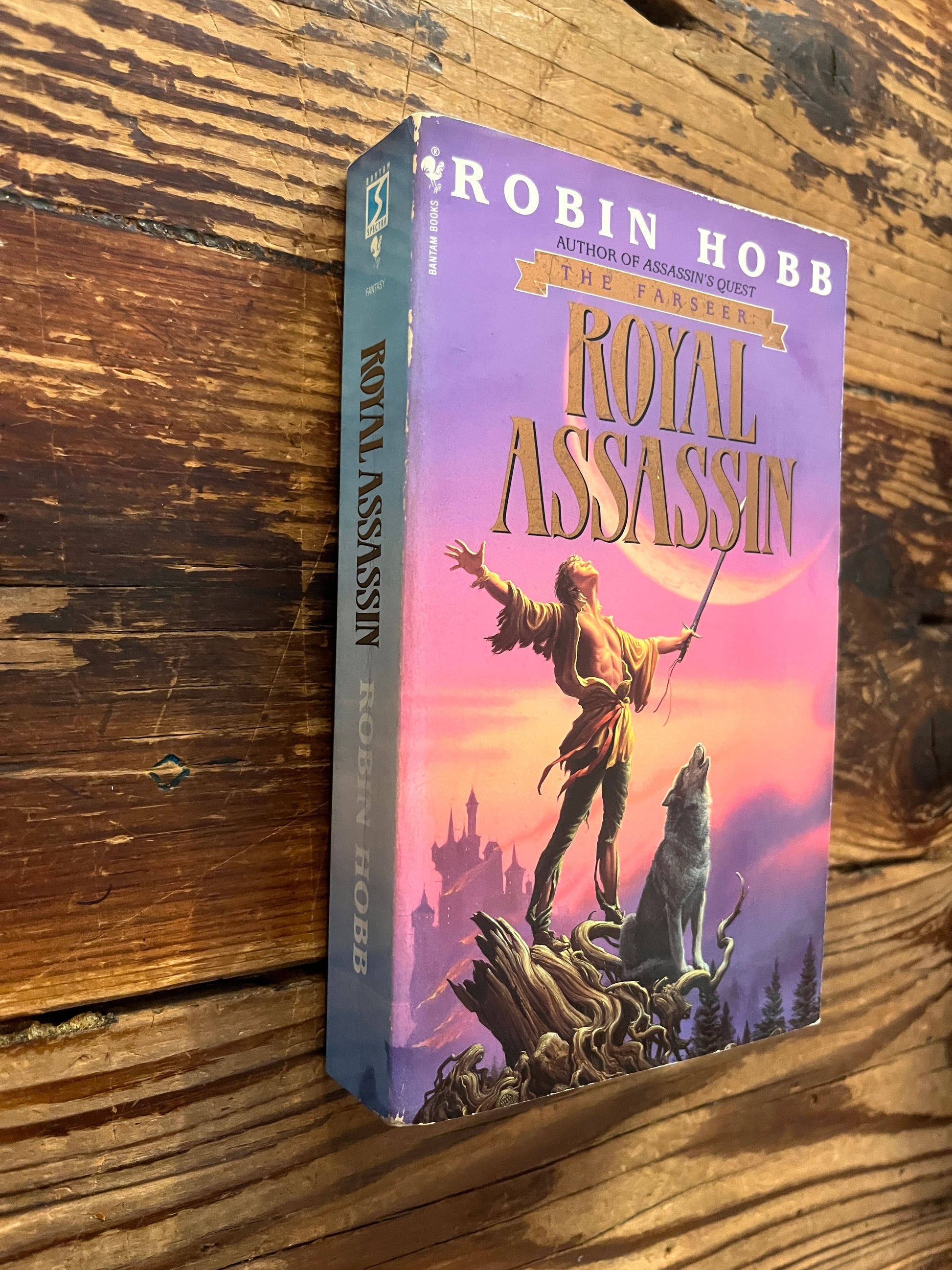 Front cover and spine of a book titled 'Royal Assassin' by Robin Hobb on a wooden surface 