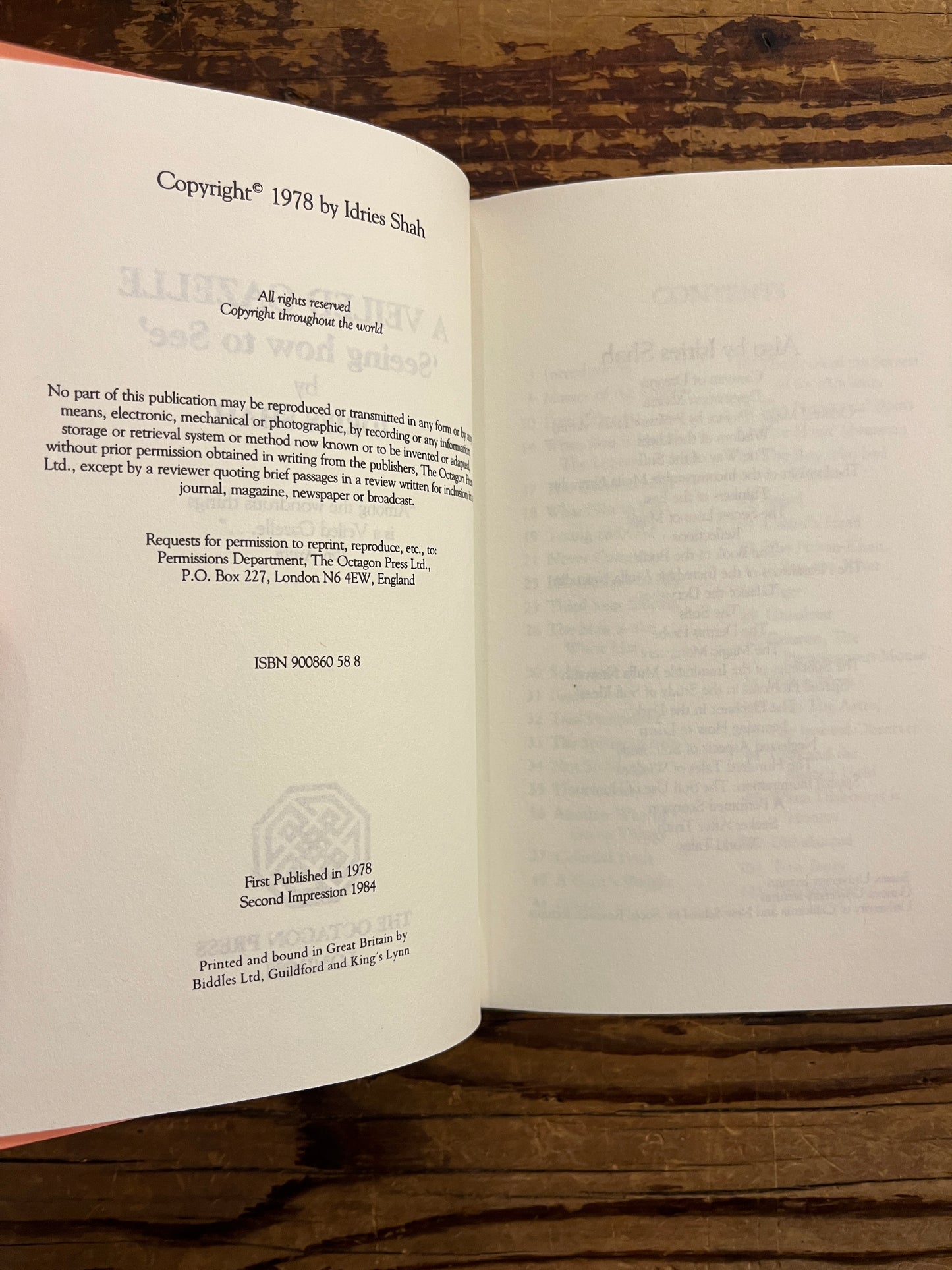 Open book titled 'A Veiled Gazette' by Idries Shah on a wooden surface