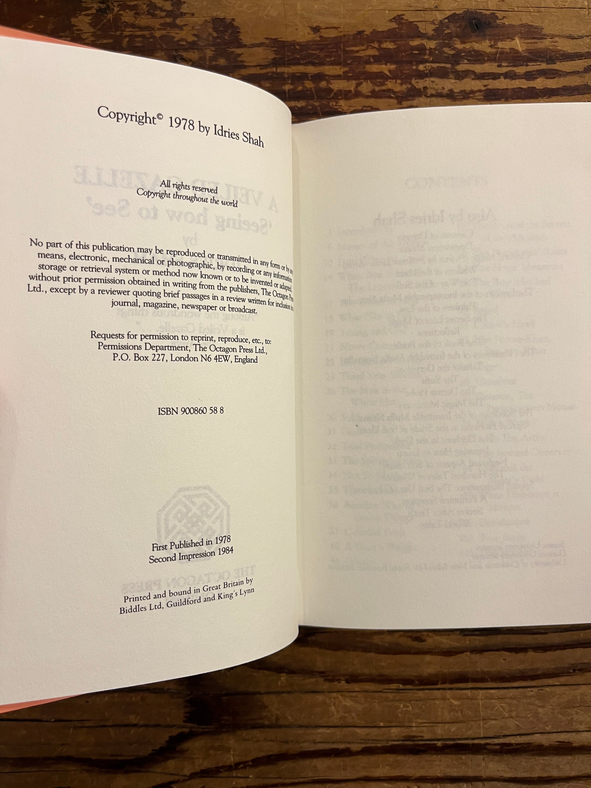 Open book titled 'A Veiled Gazette' by Idries Shah on a wooden surface