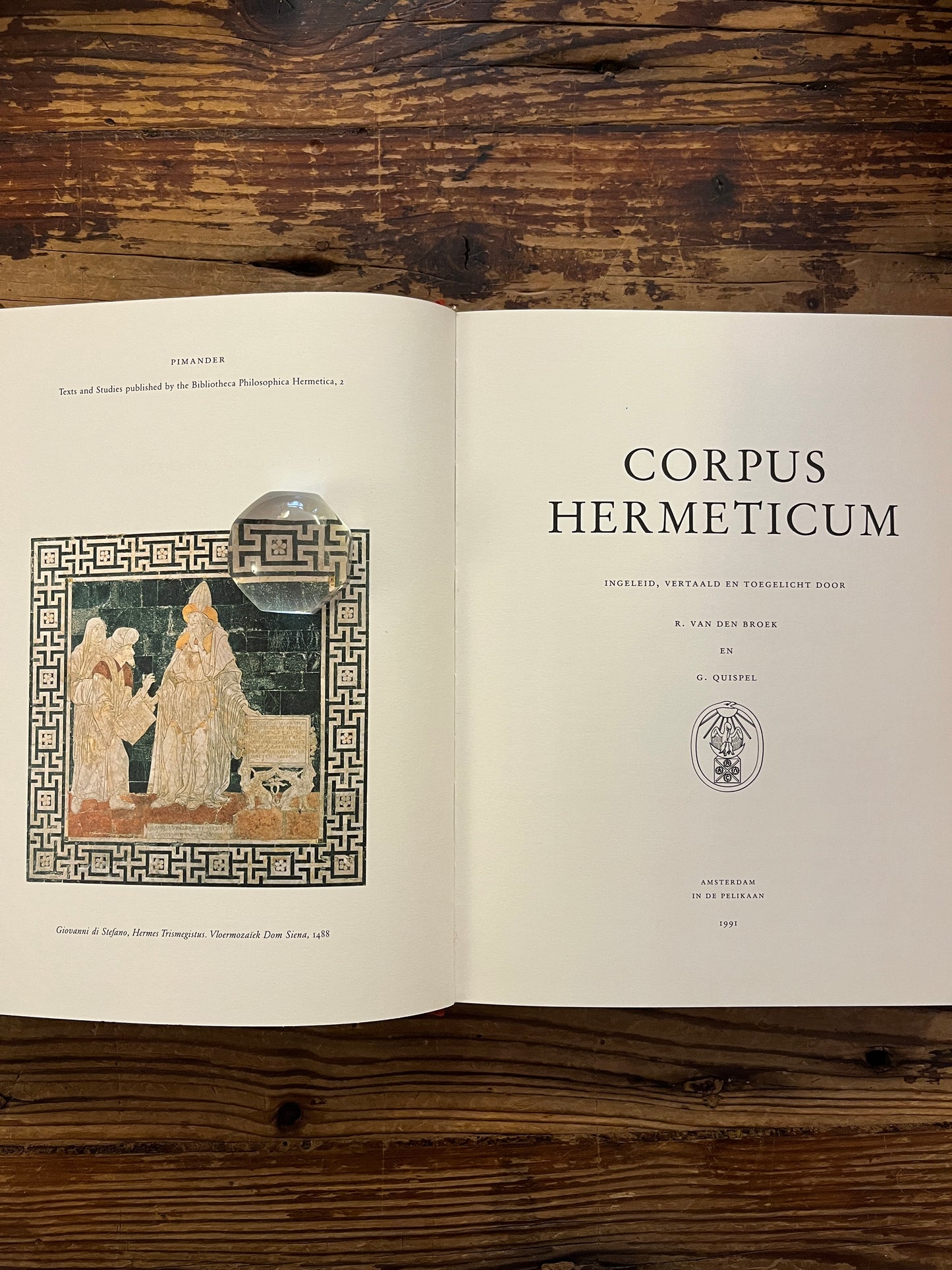 Open boek 'Corpus hermeticum' ingeleid, vertaald en toegelicht door R. van den Broek en G. Quispel, op een houten achtergrond