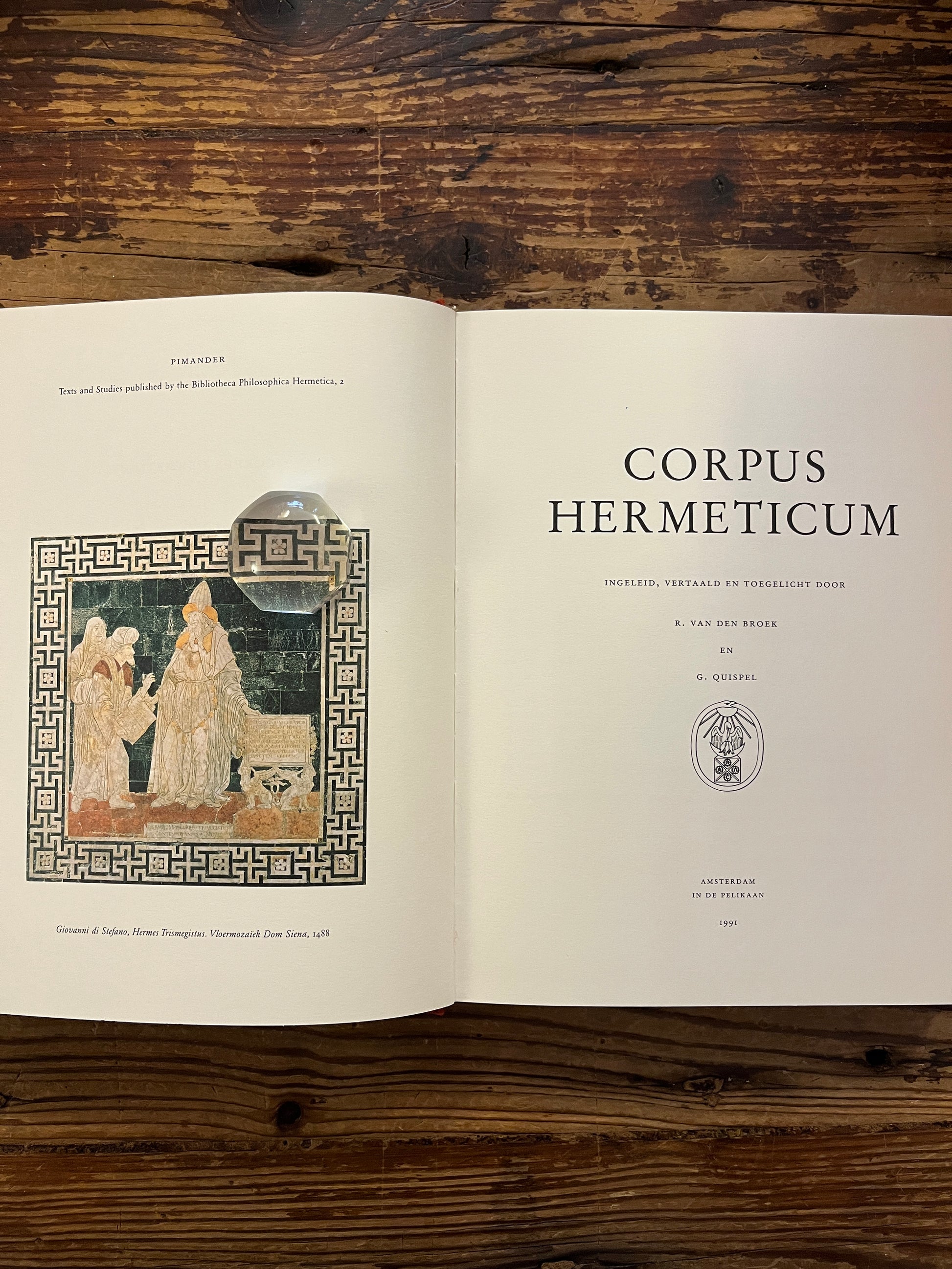 Open boek 'Corpus hermeticum' ingeleid, vertaald en toegelicht door R. van den Broek en G. Quispel, op een houten achtergrond