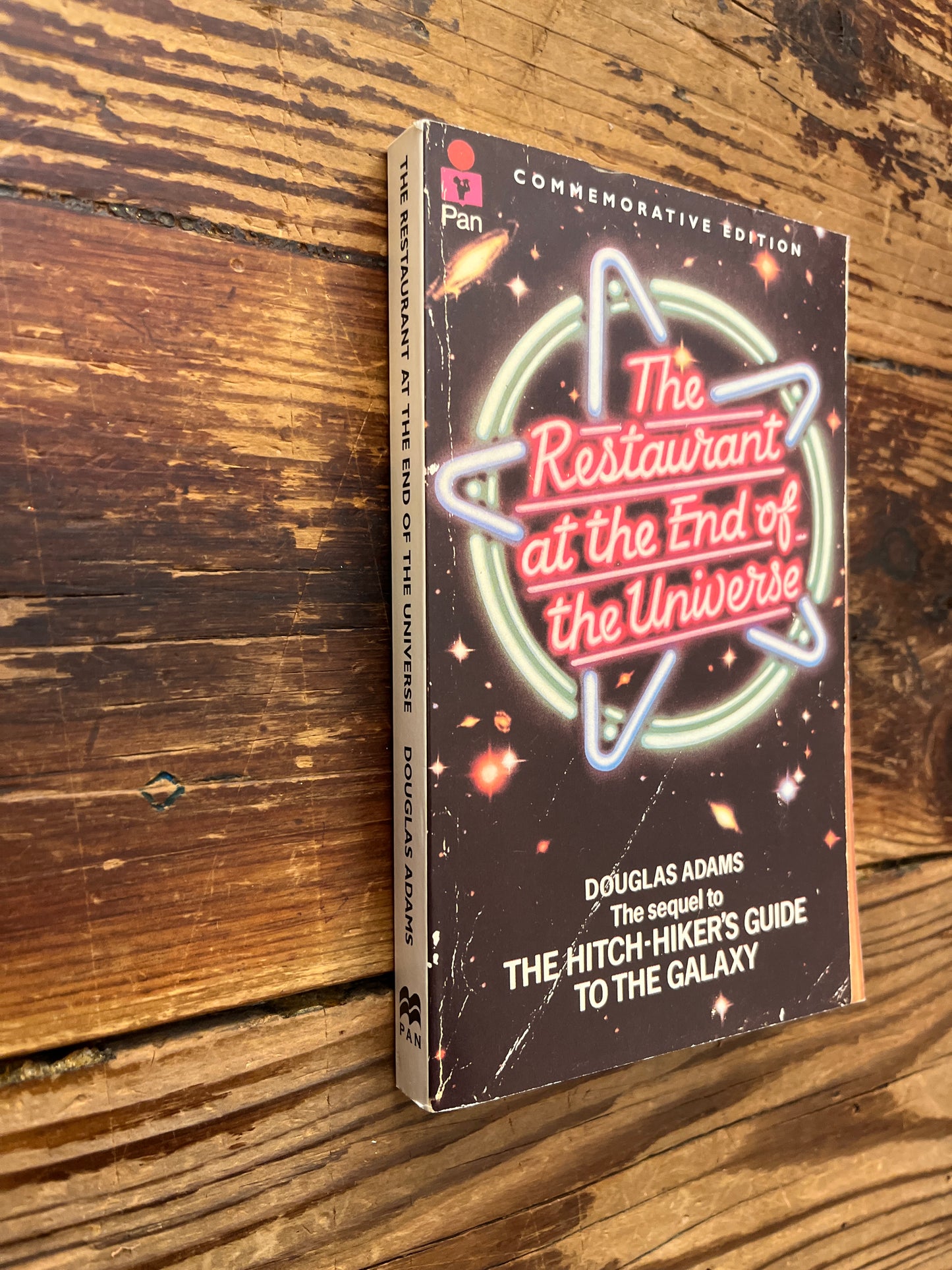Book cover of 'The Restaurant at the End of the Universe' by Douglas Adams on a wooden surface