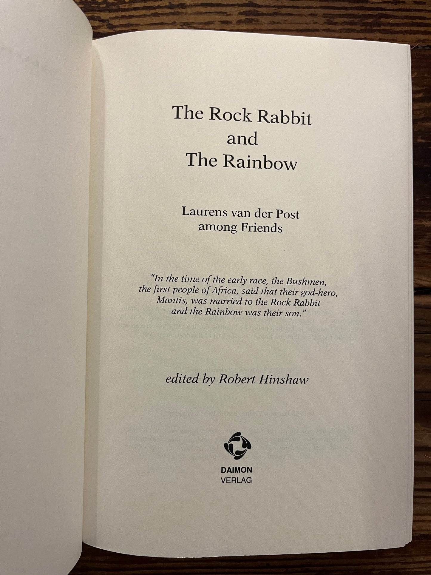 Open book with the title 'The Rock Rabbit and The Rainbow' by Laurens van der Post on a wooden surface