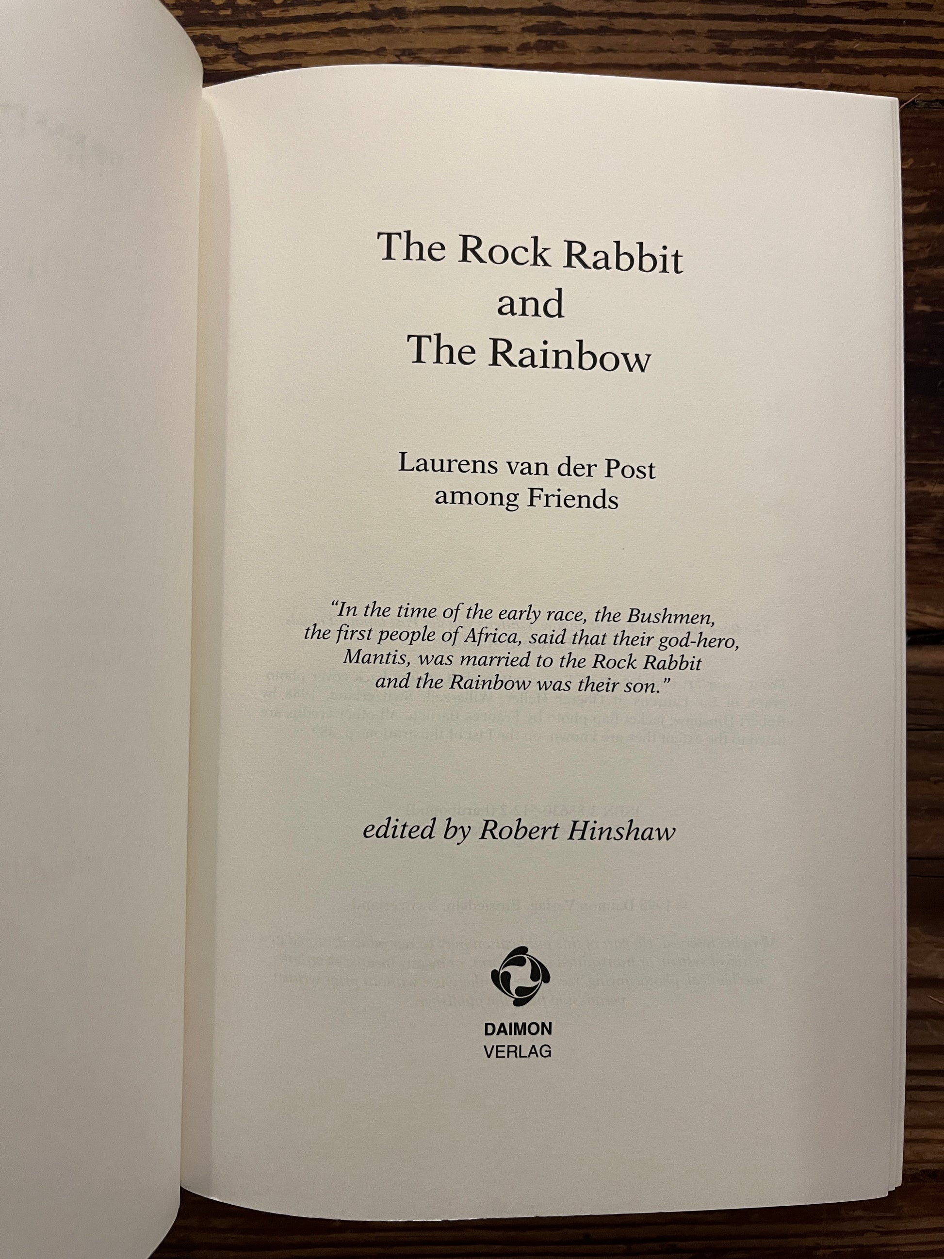 Open book with the title 'The Rock Rabbit and The Rainbow' by Laurens van der Post on a wooden surface