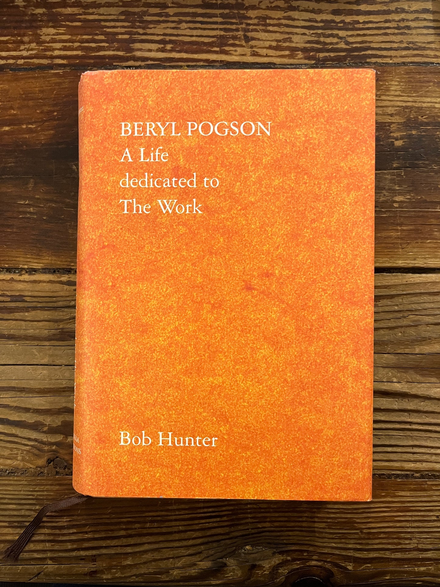 Orange book titled 'Beryl Pogson: A Life Dedicated to the Work' by Bob Hunter on a wooden surface