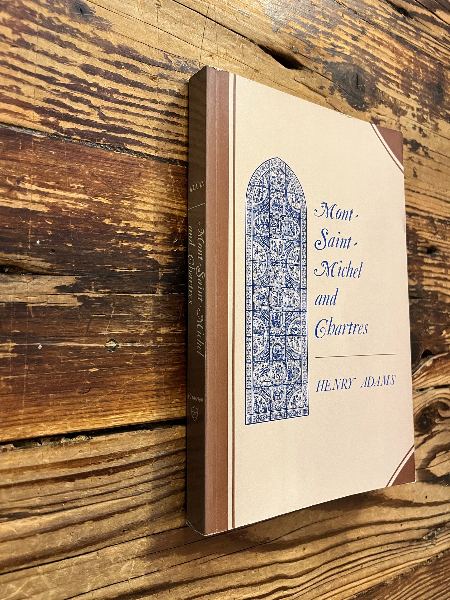 Front cover and spine of a book titled 'Mont Saint-Michel and Chartres' by Henry Adams on a wooden surface