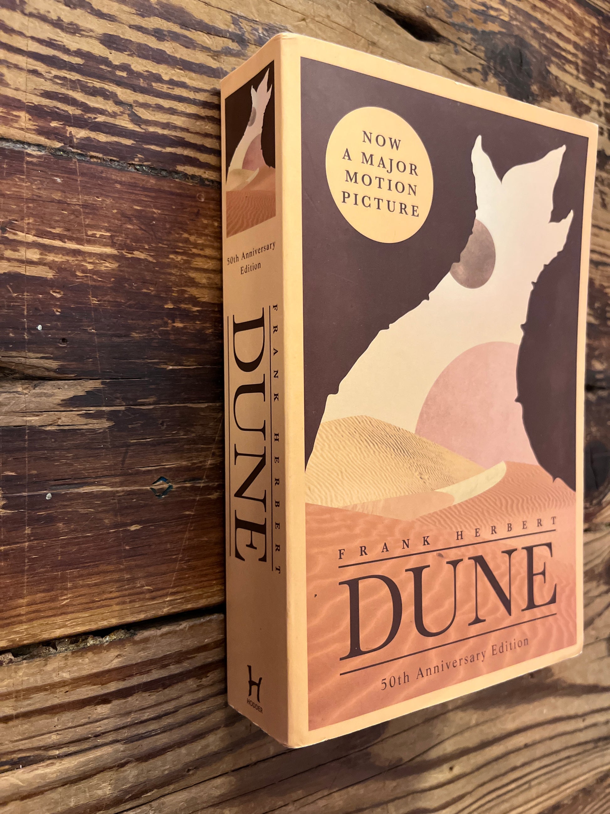 Front cover of book titled 'Dune' by Frank herbert on a wooden surface 