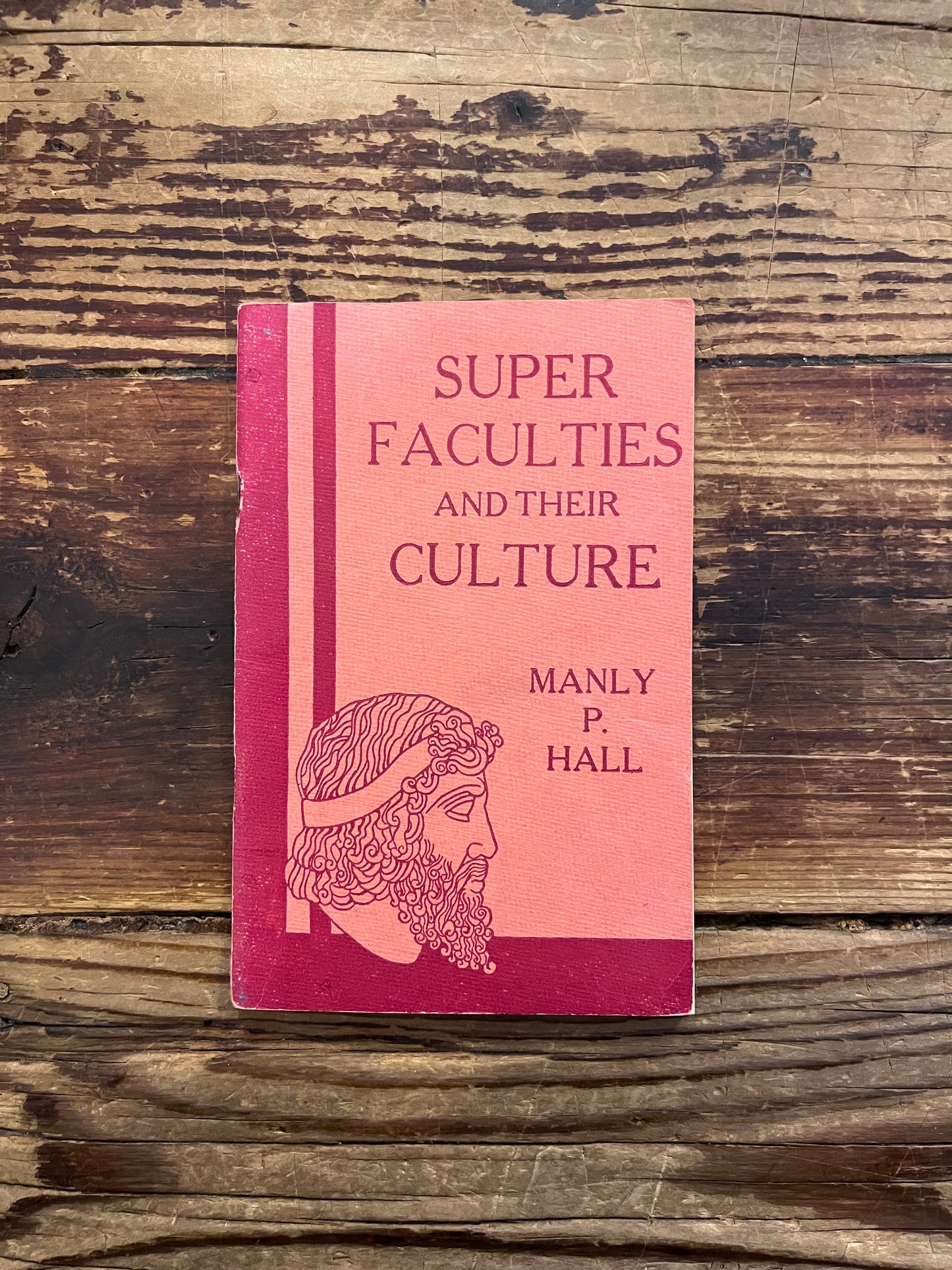 Book titled 'Super Faculties and Their Culture' by Manly P. Hall on a wooden surface