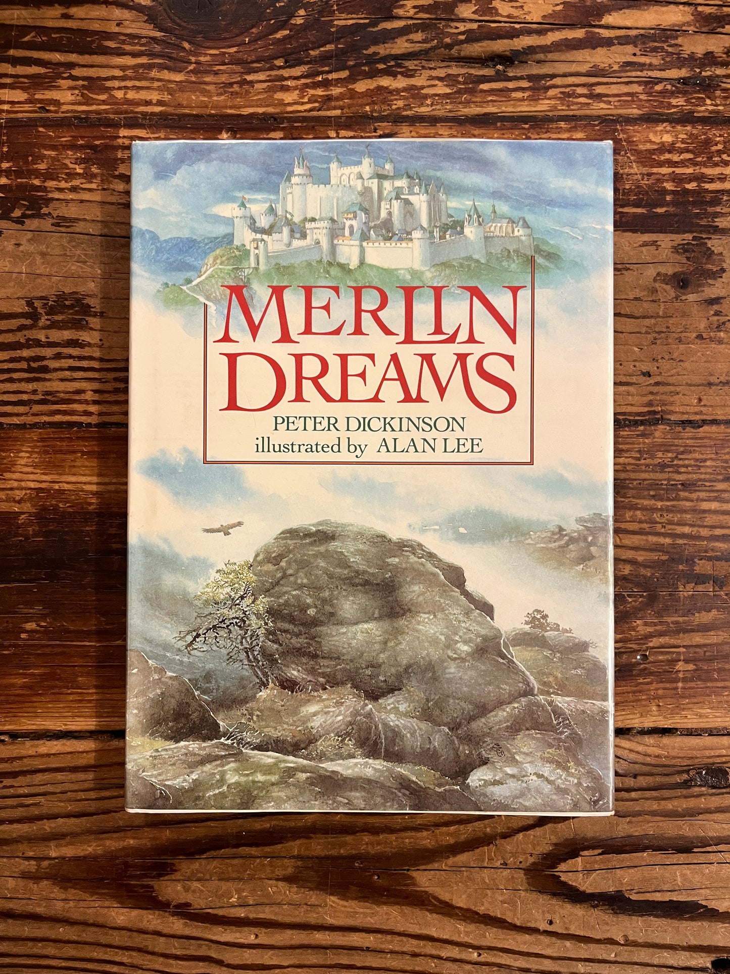 Cover of book titled 'Merlin Dreams' by Peter Dickinson and illustrated by Alan Lee on a wooden surface 