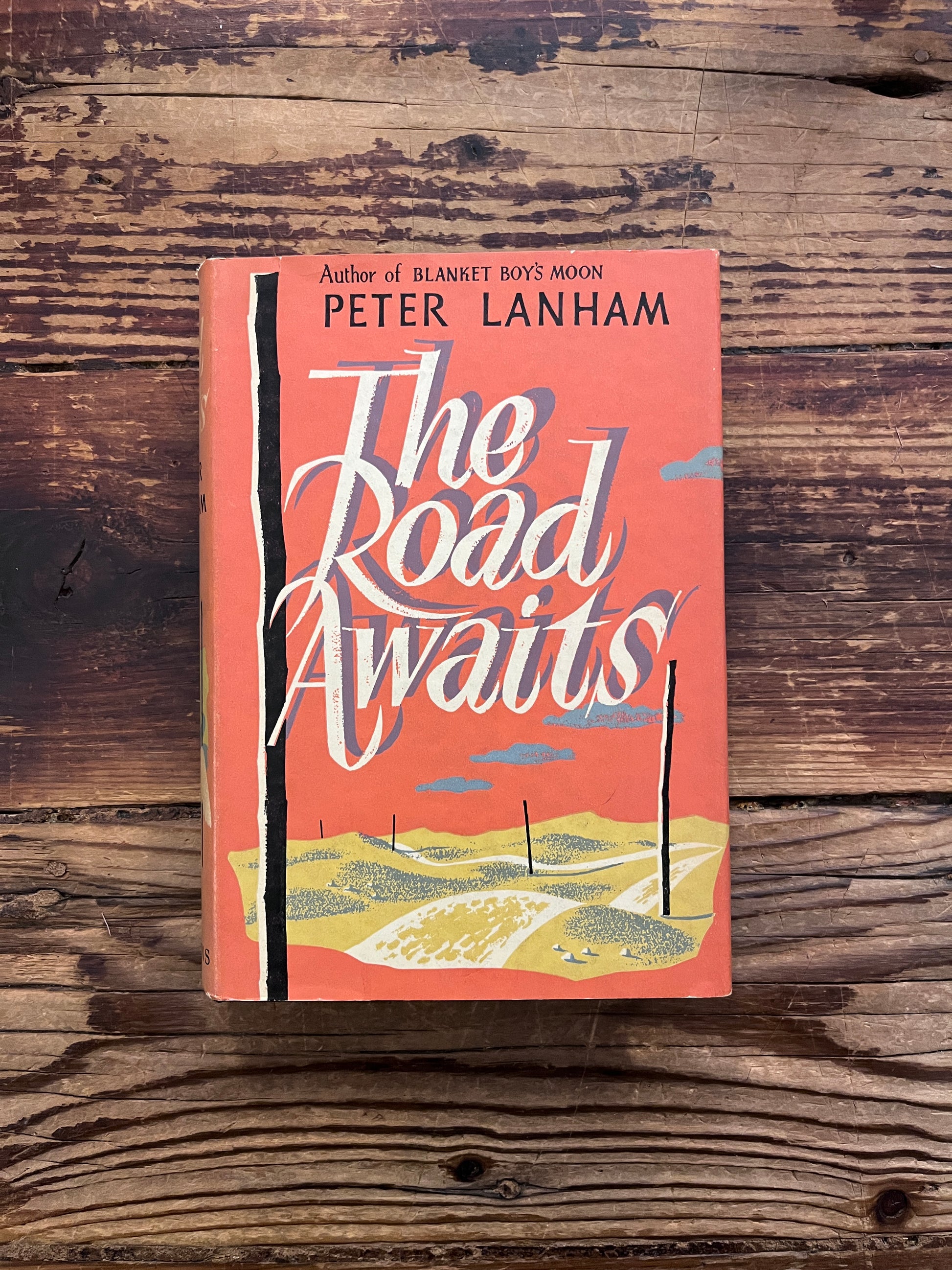 Book titled 'The Road Waits' by Peter Lanham on a wooden surface