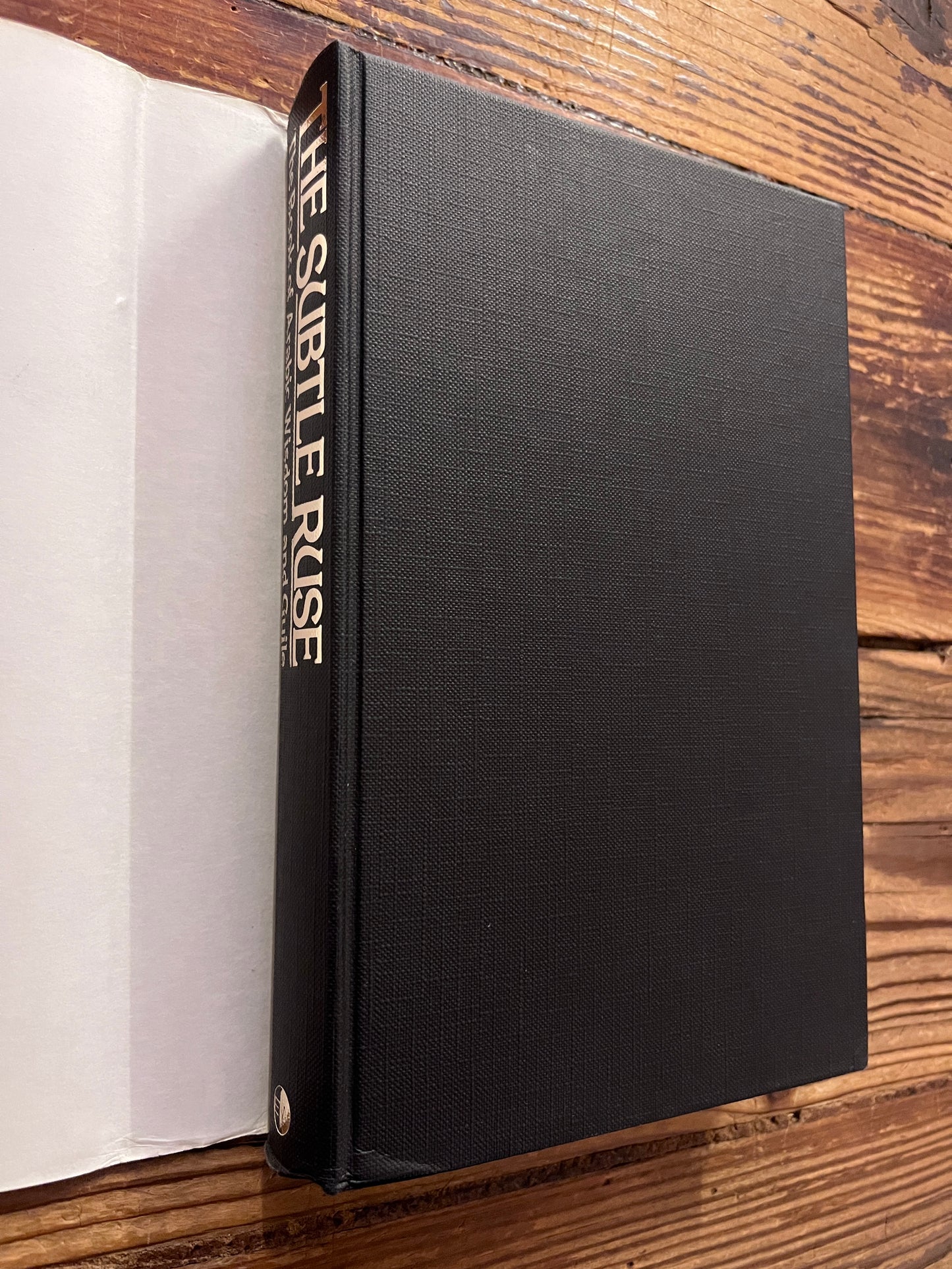 This image features the spine and front cover without dust jacket of a hardcover book titled "The Subtle Ruse, The Book of Arabic Wisdom and Guile," translated by Rene R. Khawam on a wooden surface