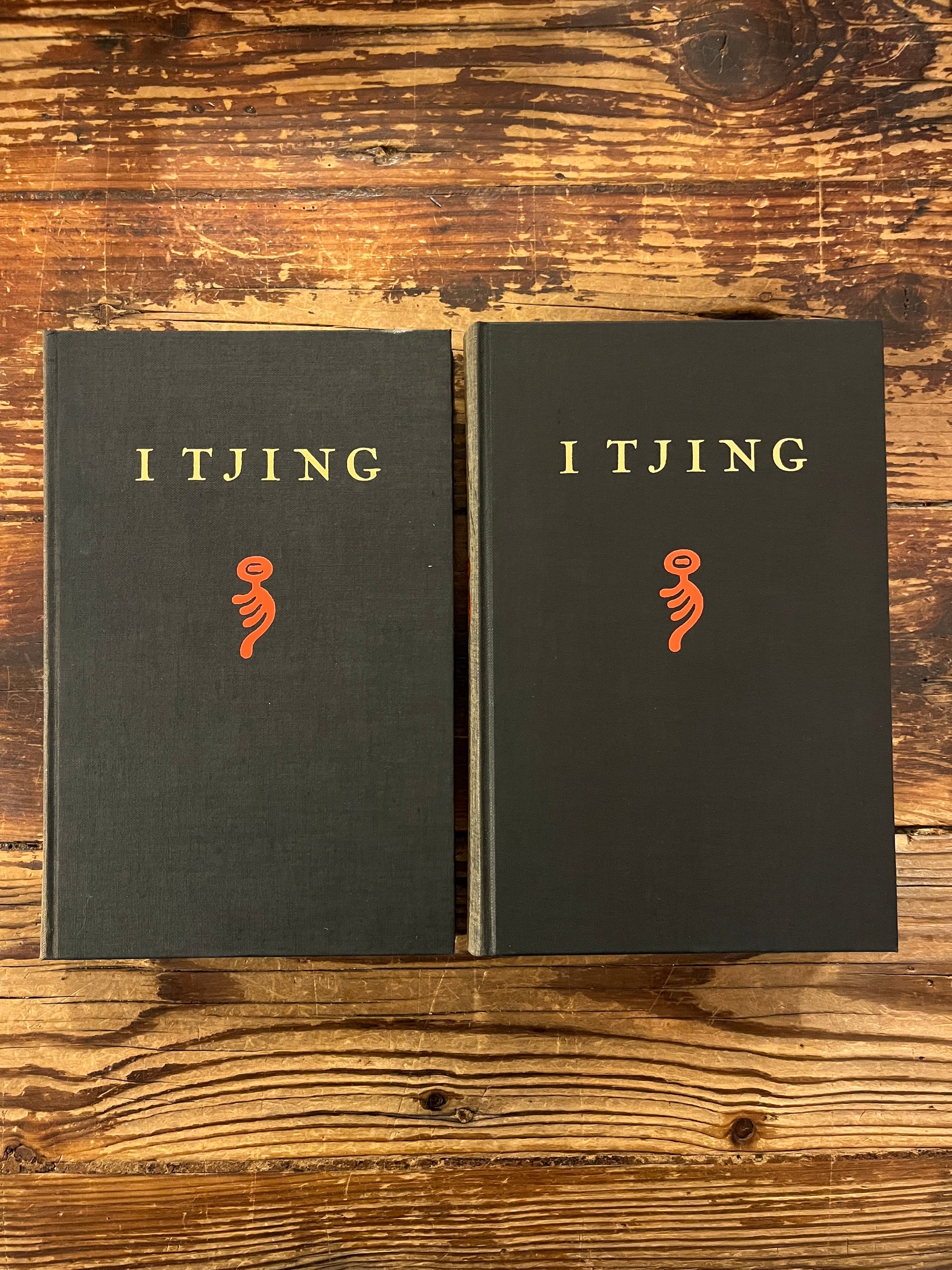 twee boeken met de titel 'I Tjing: Het Boek Der Veranderingen' op een houten achtergrond