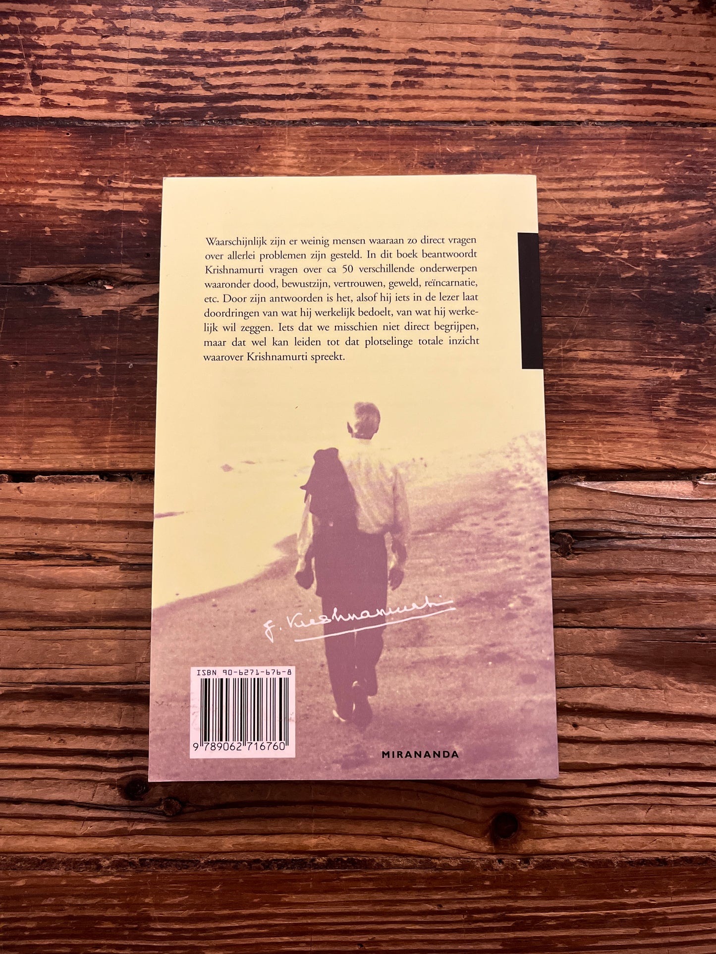 Achterkant boek met de titel 'antwoord op vragen' door krishnamurti op een houten achtergrond 