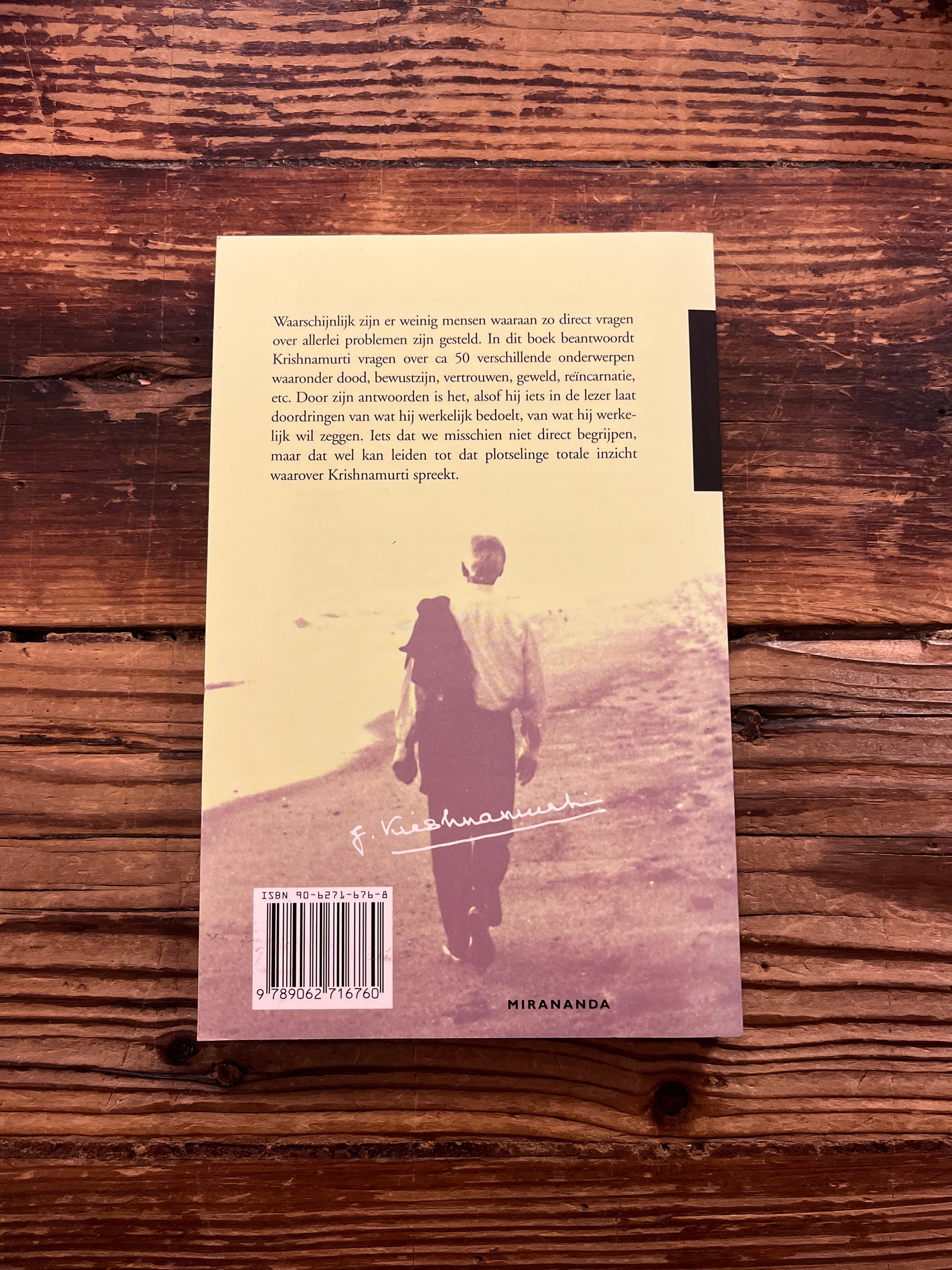 Achterkant boek met de titel 'antwoord op vragen' door krishnamurti op een houten achtergrond 