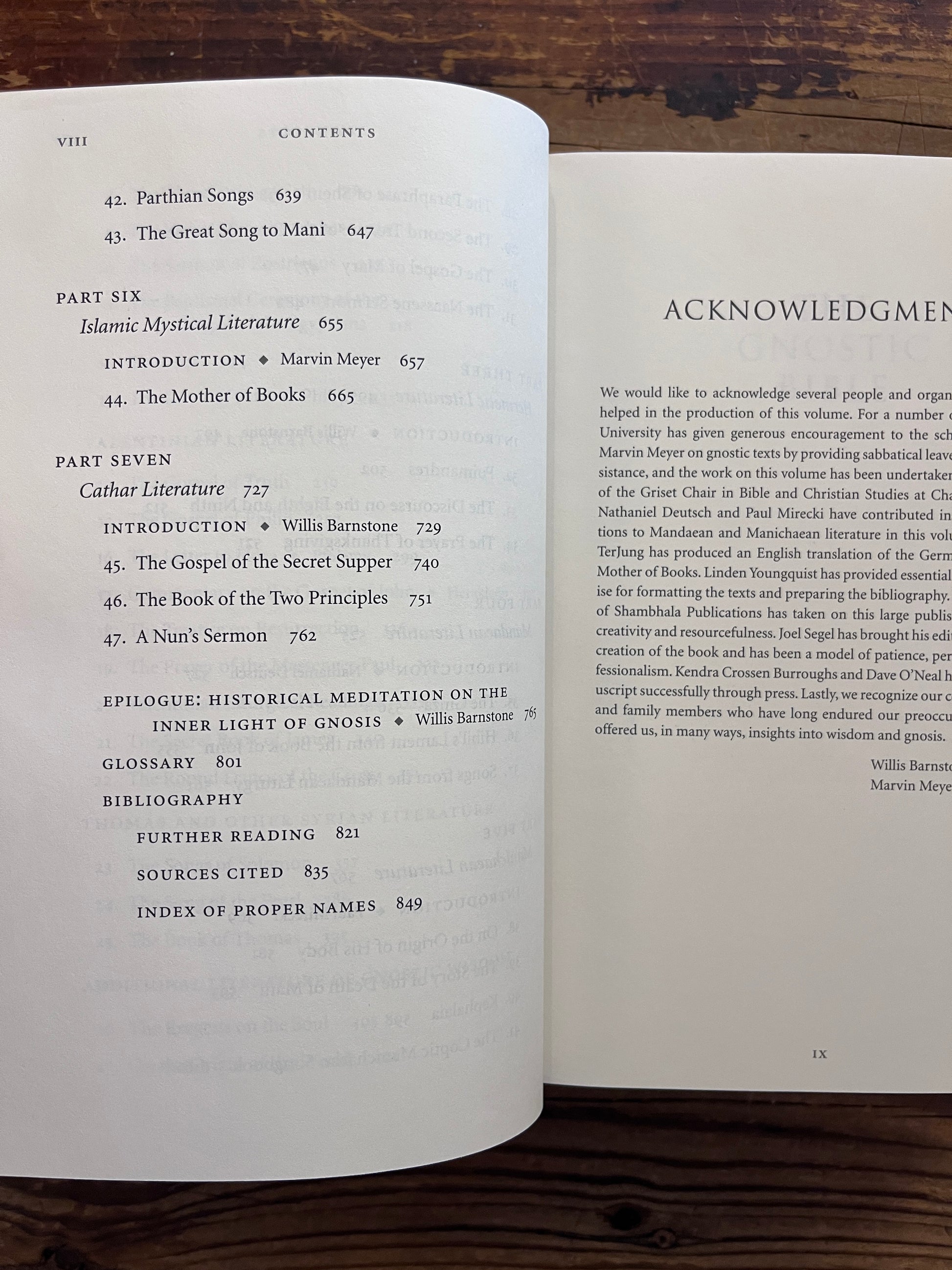 Open book titled 'he Gnostic Bible' edited by Willis Barnstone and Marvin Meyer, on a wooden surface