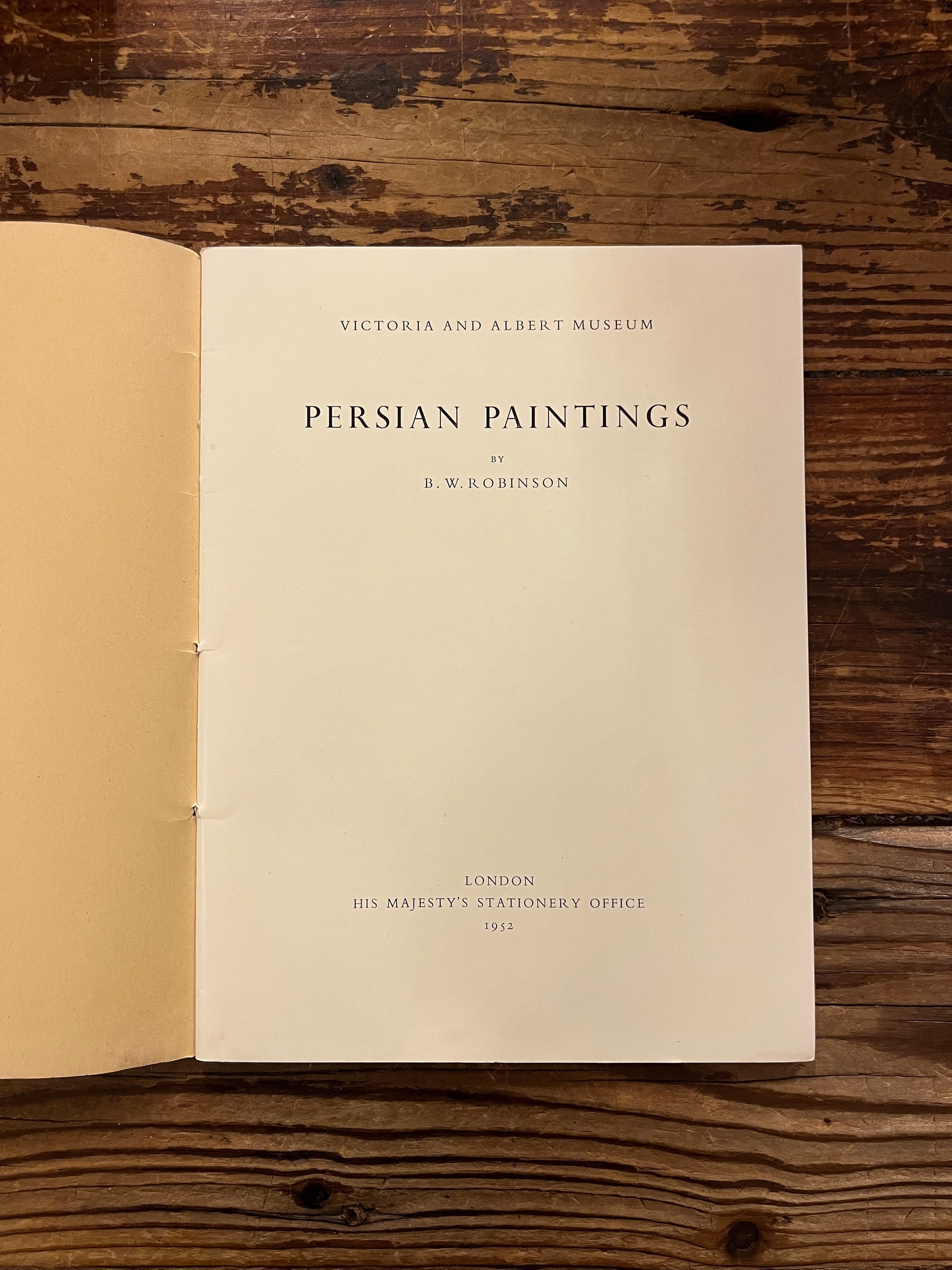 Open book titled 'Persian Paintings' by A.W. Robinson on a wooden surface