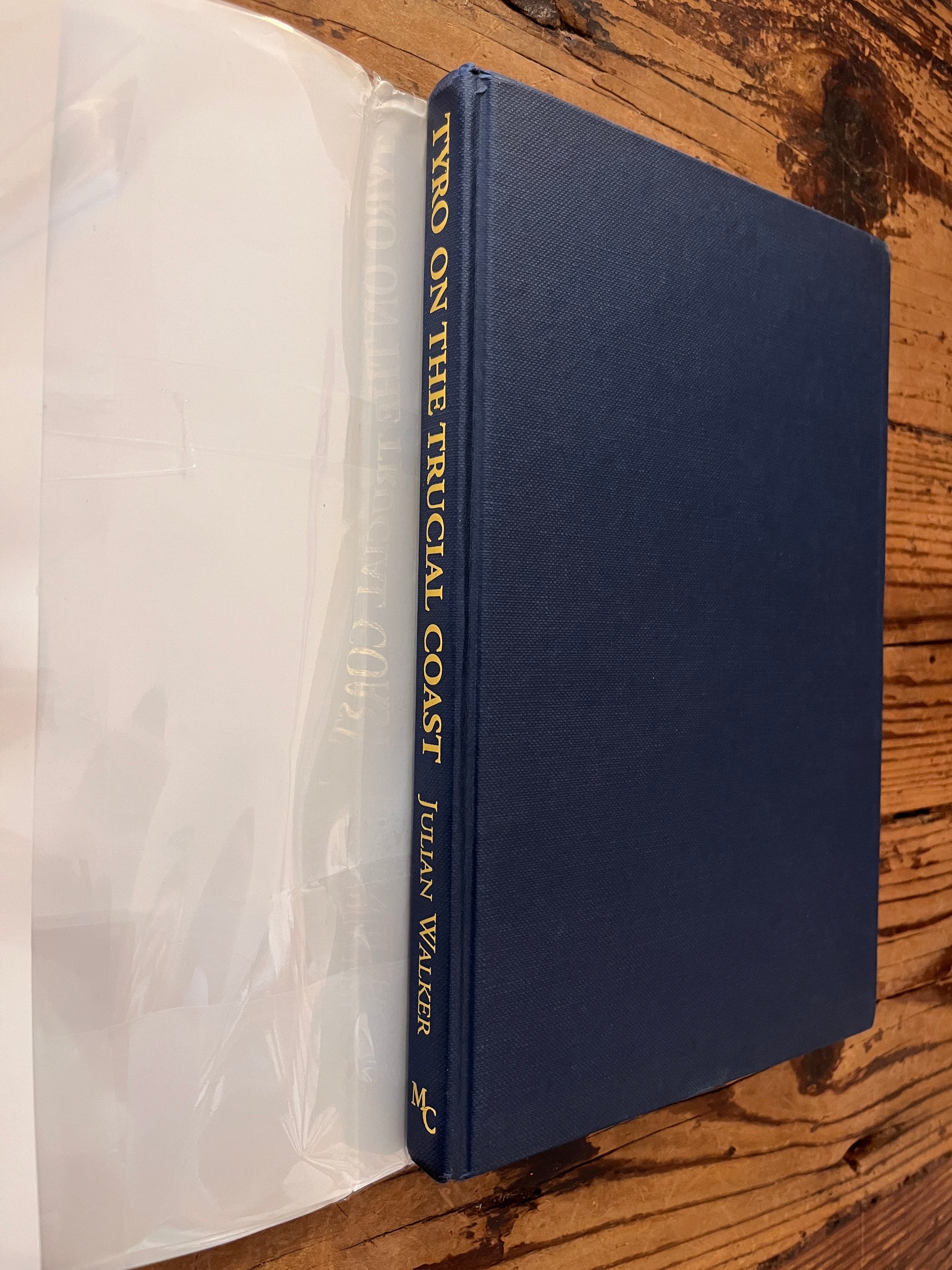 Front cover and spine of book without dust jacket titled 'Tyro on the Trucial Coast' by Julian Walker on a wooden surface