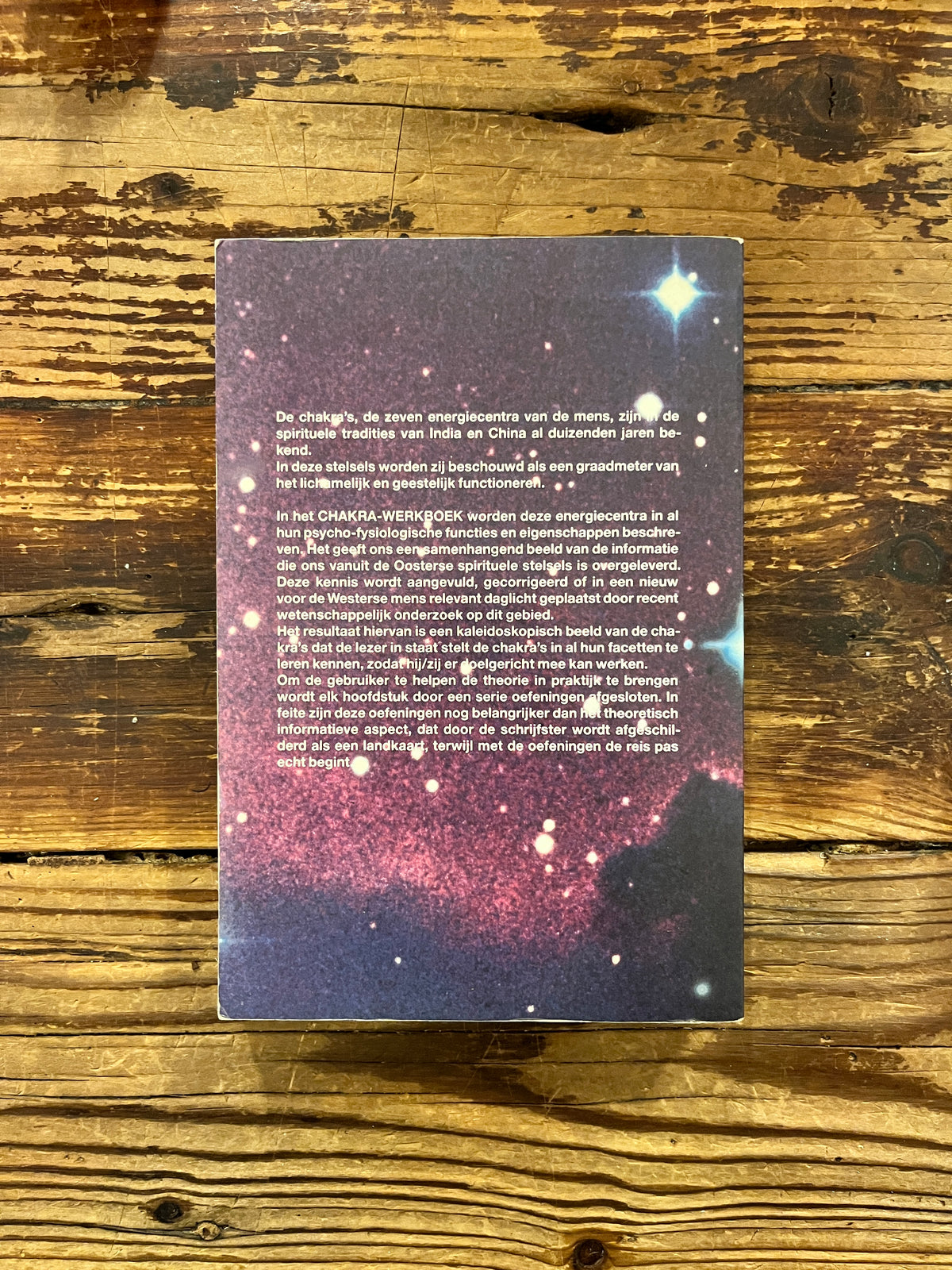 Achterkant van boek met de titel 'Chakra werkboek' door Andrea Judith op een houten achtergrond 