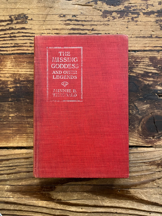 Front cover of a book titled 'the missing Goddess and other legends' by Minnie Theobald on a wooden surface