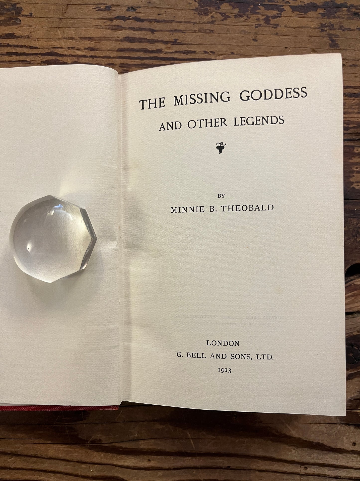Open book titled 'the missing Goddess and other legends' by Minnie Theobald on a wooden surface