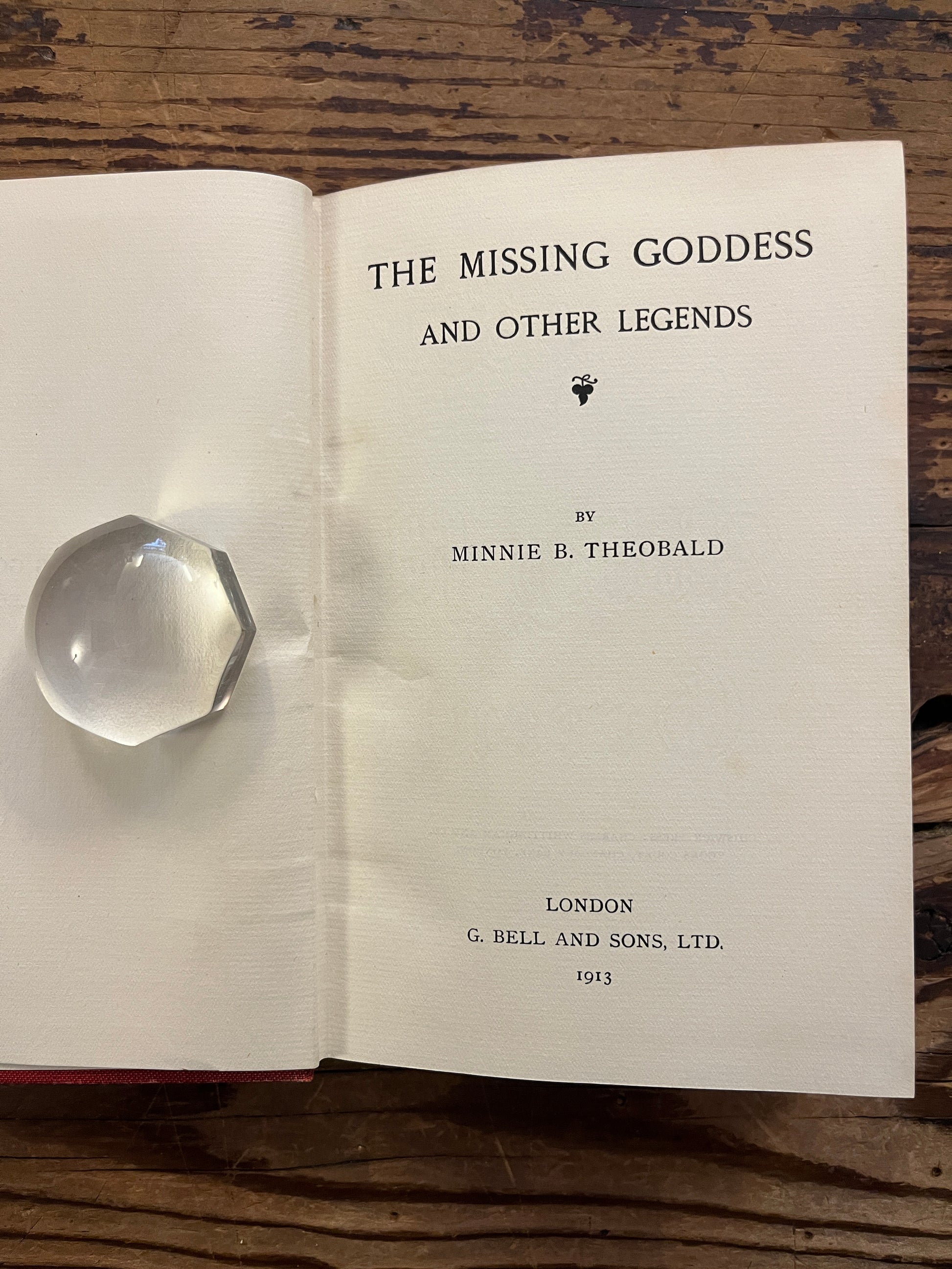 Open book titled 'the missing Goddess and other legends' by Minnie Theobald on a wooden surface