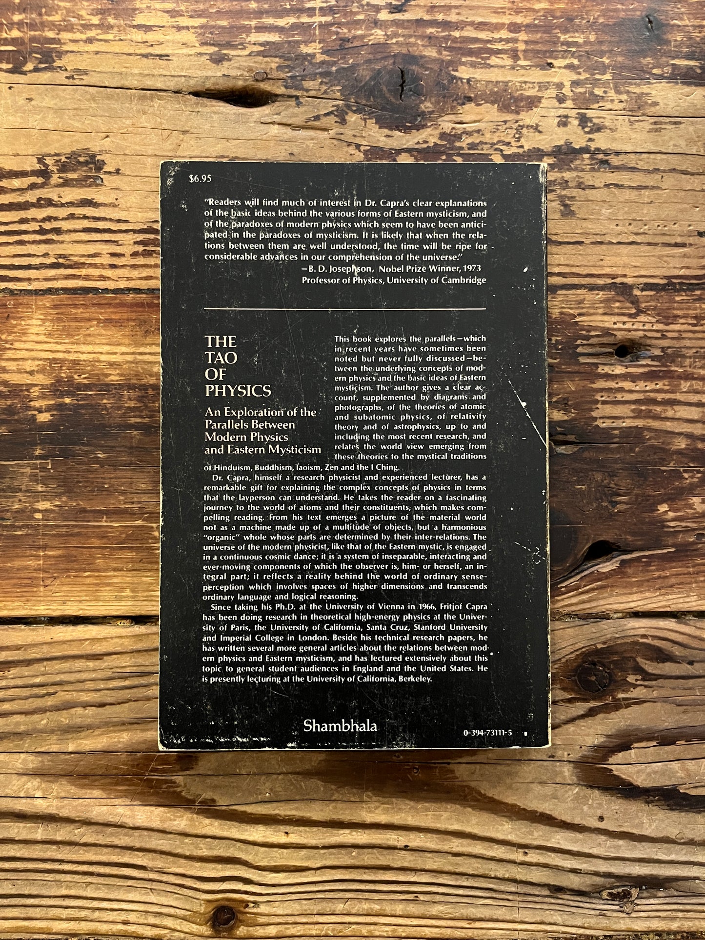 Back cover book titled 'The Tao of Physics' by Fritjof Capra on a wooden surface