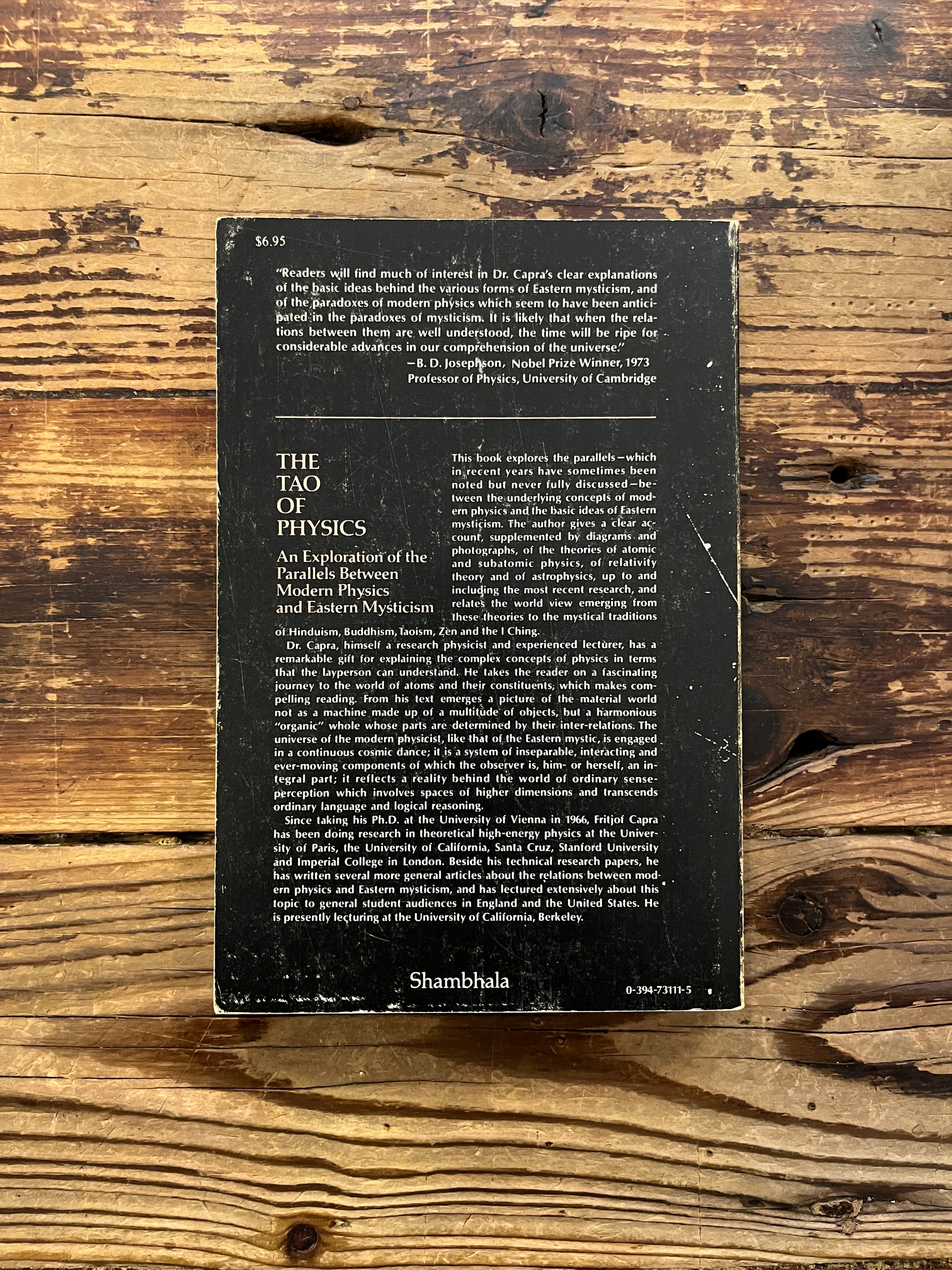 Back cover book titled 'The Tao of Physics' by Fritjof Capra on a wooden surface