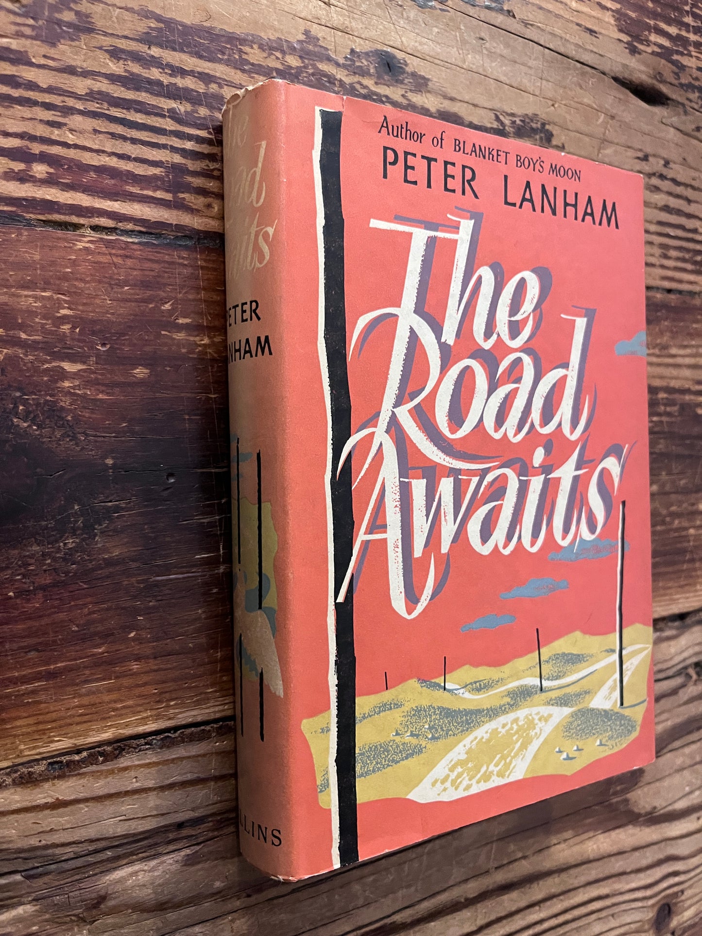 Book titled 'The Road Waits' by Peter Lanham on a wooden surface
