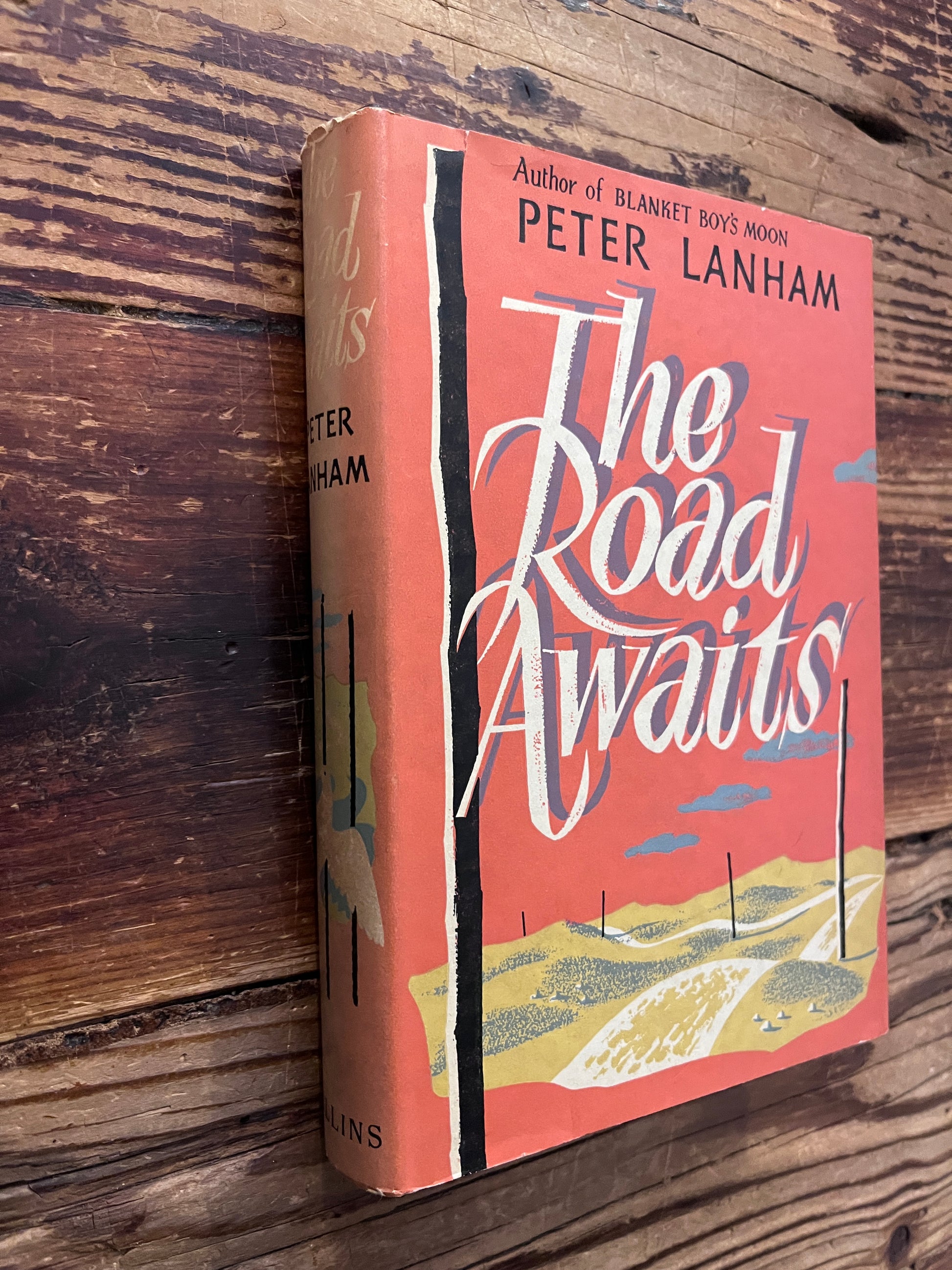 Book titled 'The Road Waits' by Peter Lanham on a wooden surface