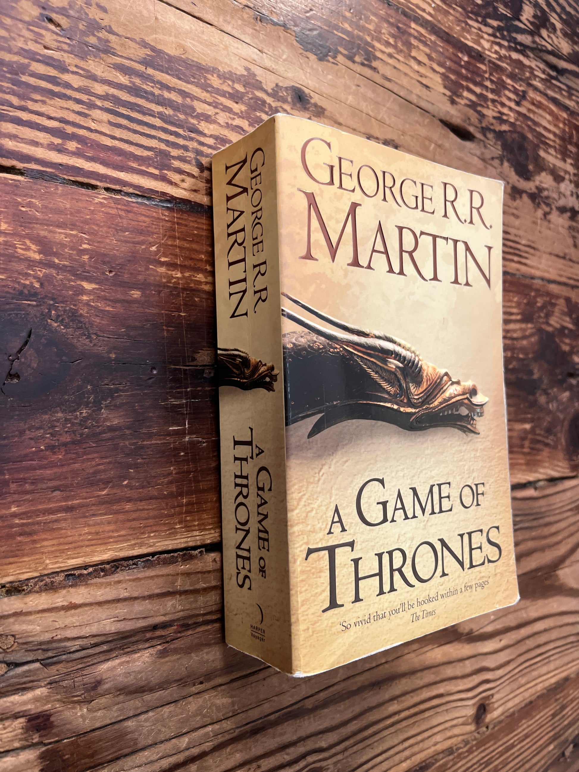 Spine and front cover of book titled 'A Game of Thrones' by George R.R. Martin on a wooden surface