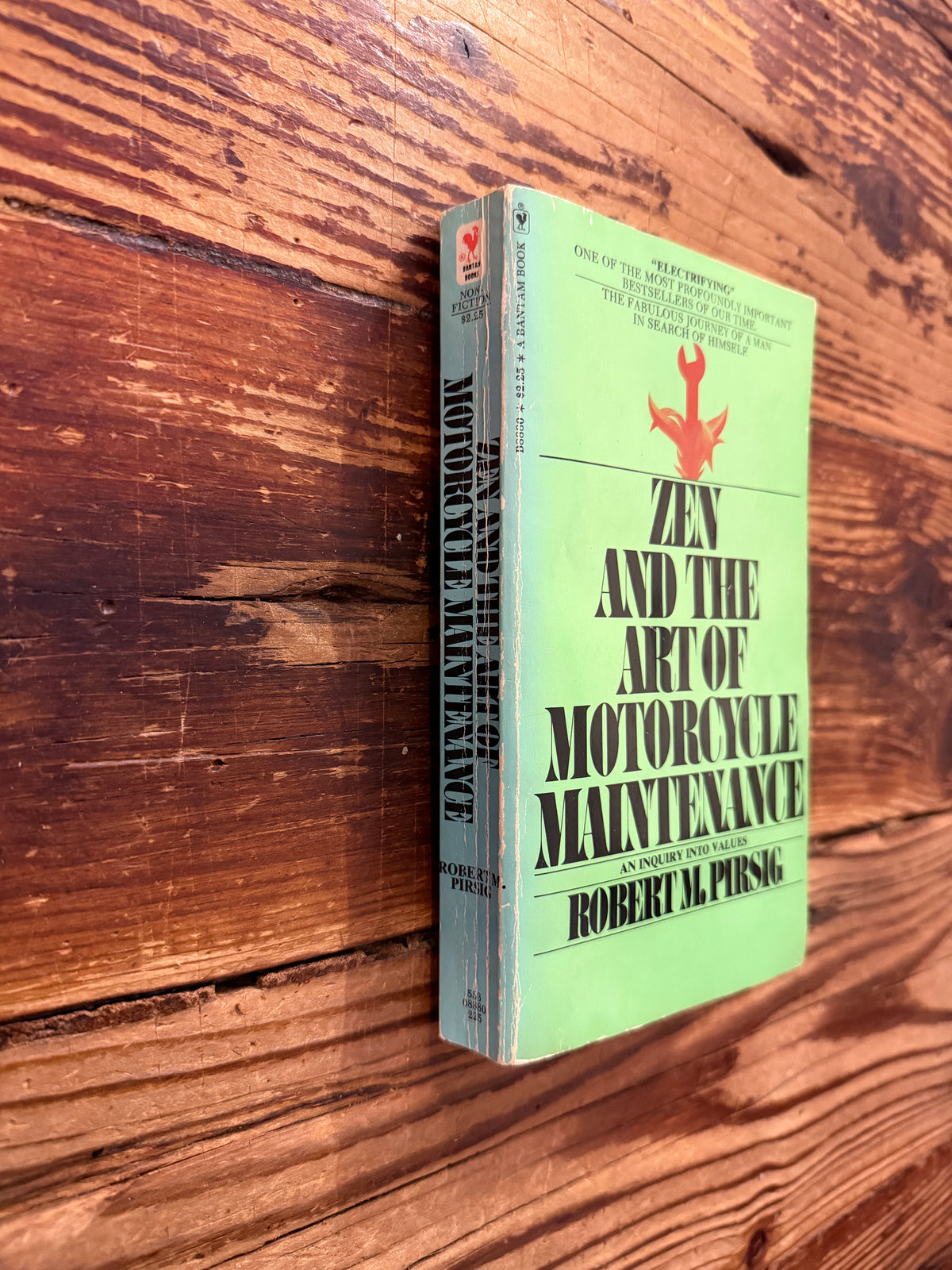 Front cover and spine of a book titled 'Zen and the Art of Motorcycle Maintenance' by Robert M. Pirsig on a wooden surface