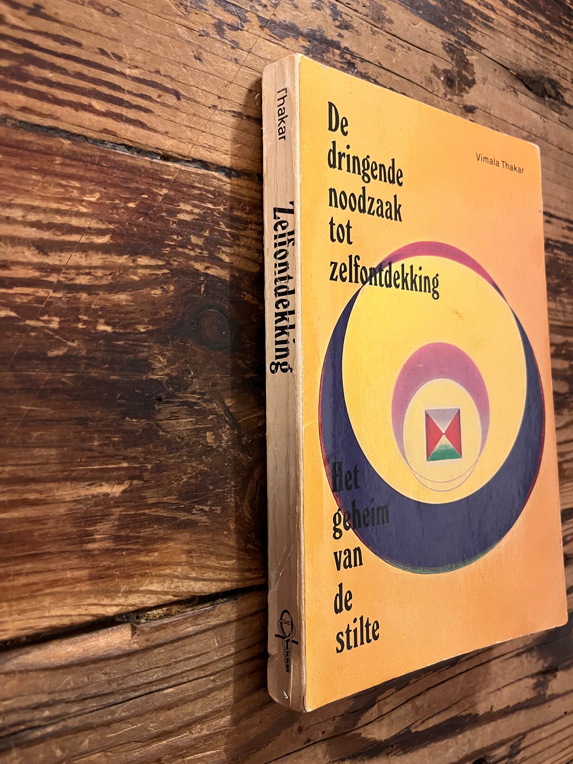 Rug van boek met de titel 'de dringende noodzaak tot zelfontdekking' door Vimala Thakar op een houten achtergrond 