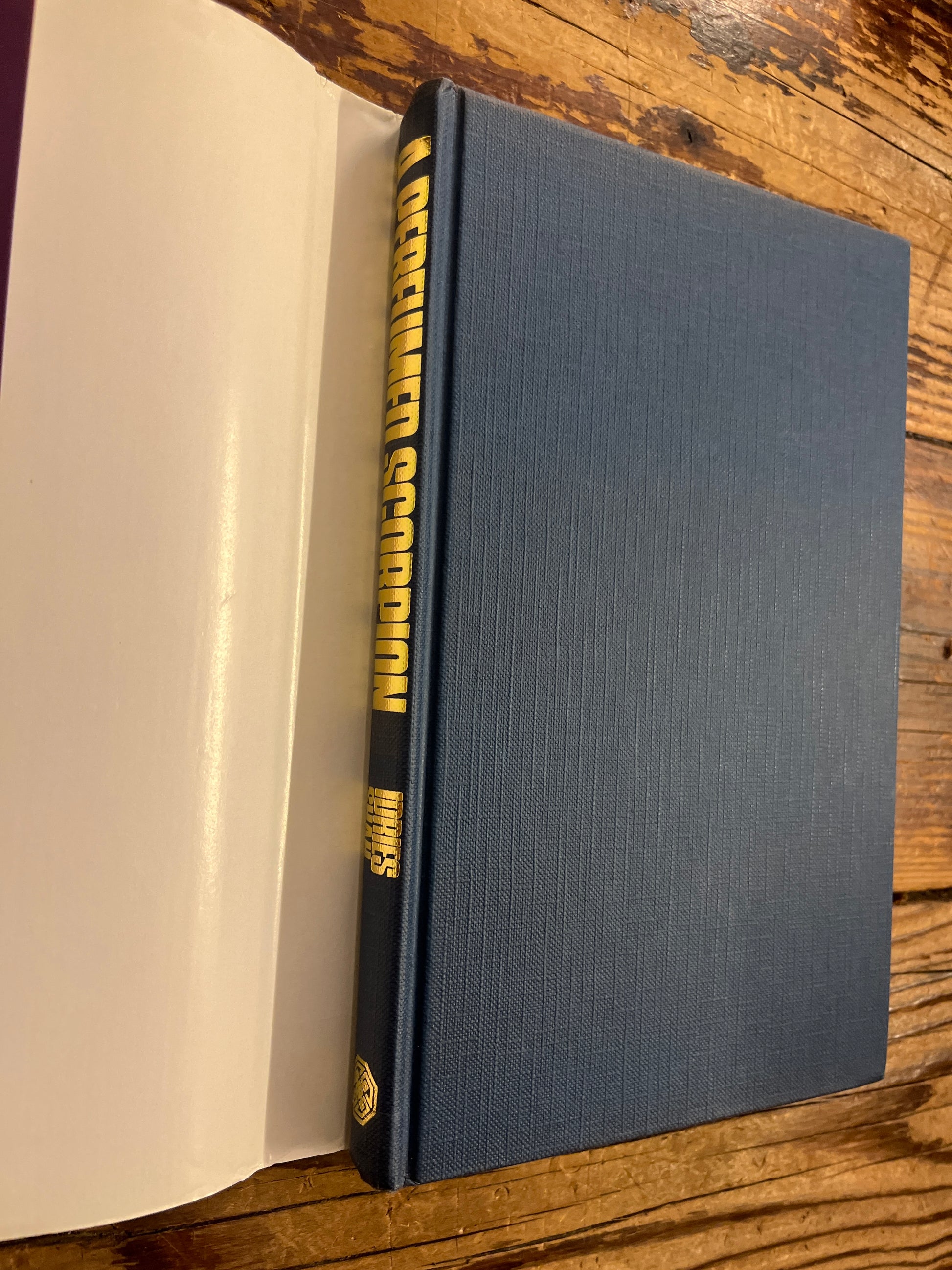 Blue book titled 'A Perfumed Scorpion' by Idries Shah with gold spine on a wooden surface