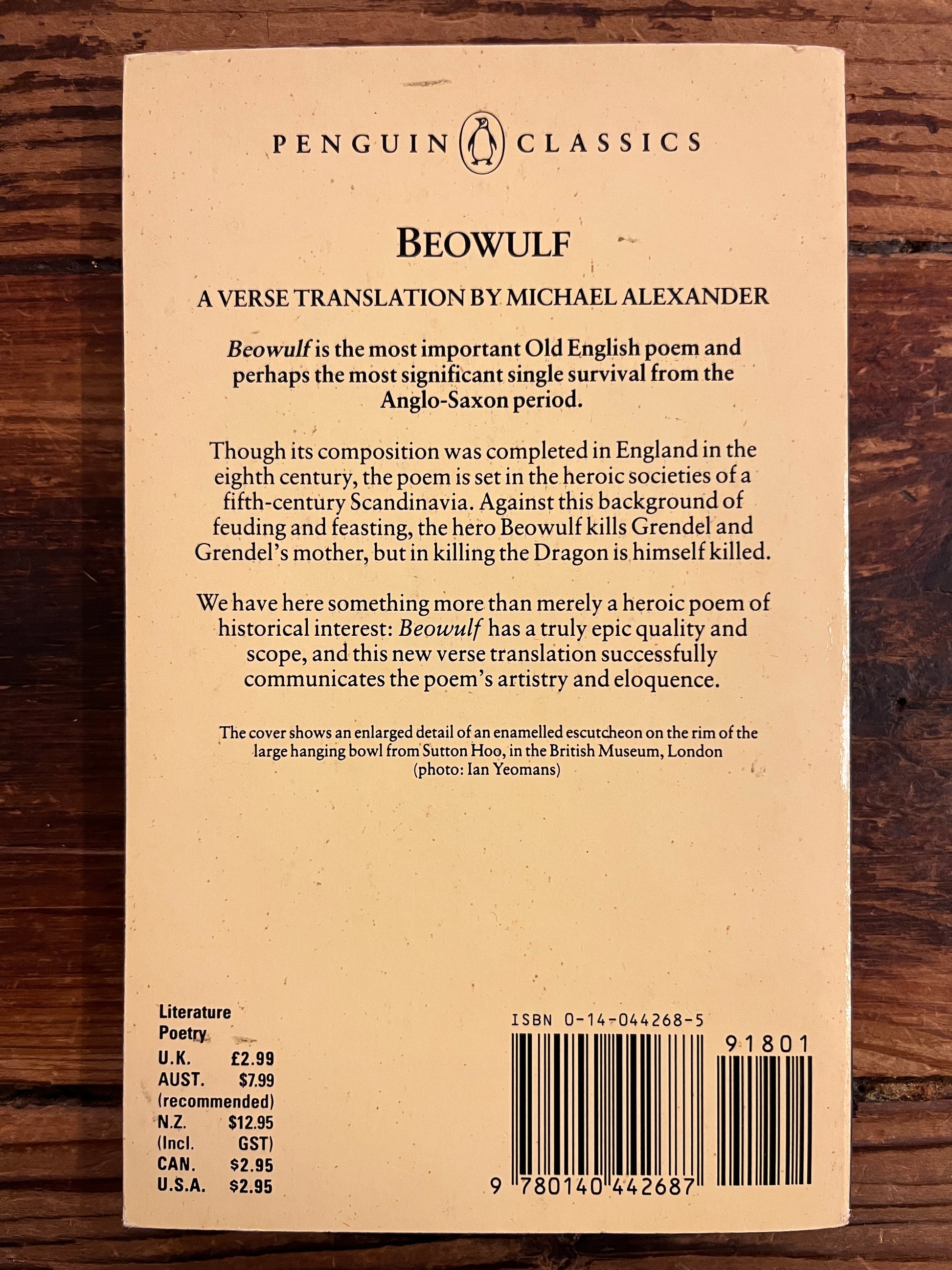 Back cover of a book titled 'Beowulf' by Michael Alexander on a wooden surface