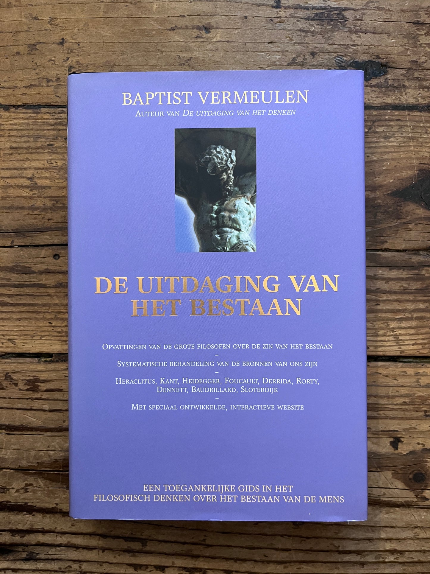 foto van de cover van het boek "De uitdaging van het bestaan"op houten achtergrond