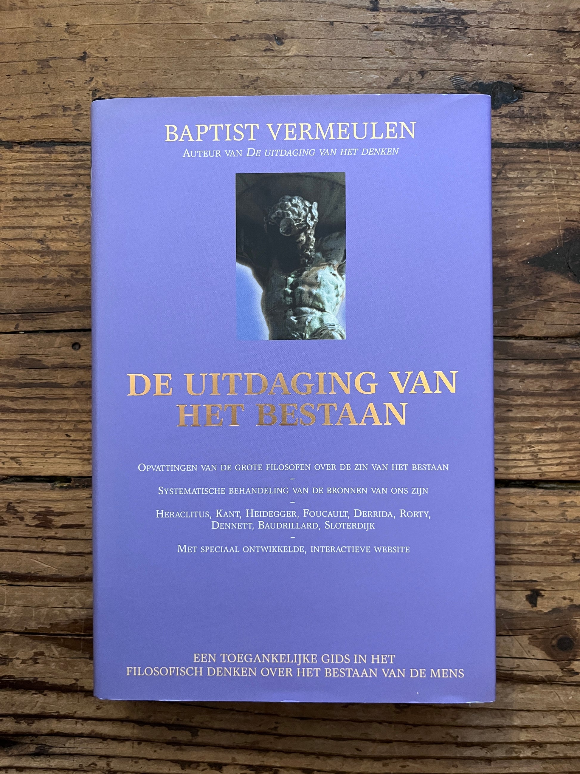 foto van de cover van het boek "De uitdaging van het bestaan"op houten achtergrond