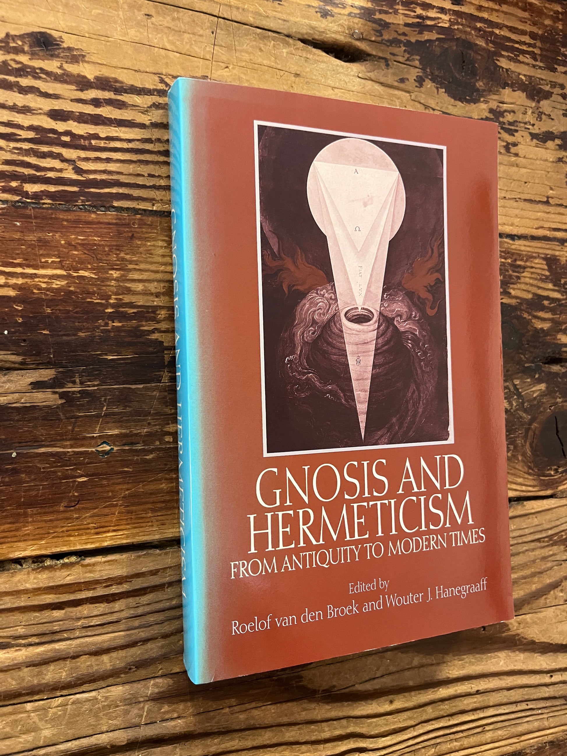 Front cover and spine of a book titled 'Gnosis and Hermeticism: From Antiquity to Modern Times' edited by Roelof van den Broek and Wouter J. Hanegraaff op een houten achtergrond 