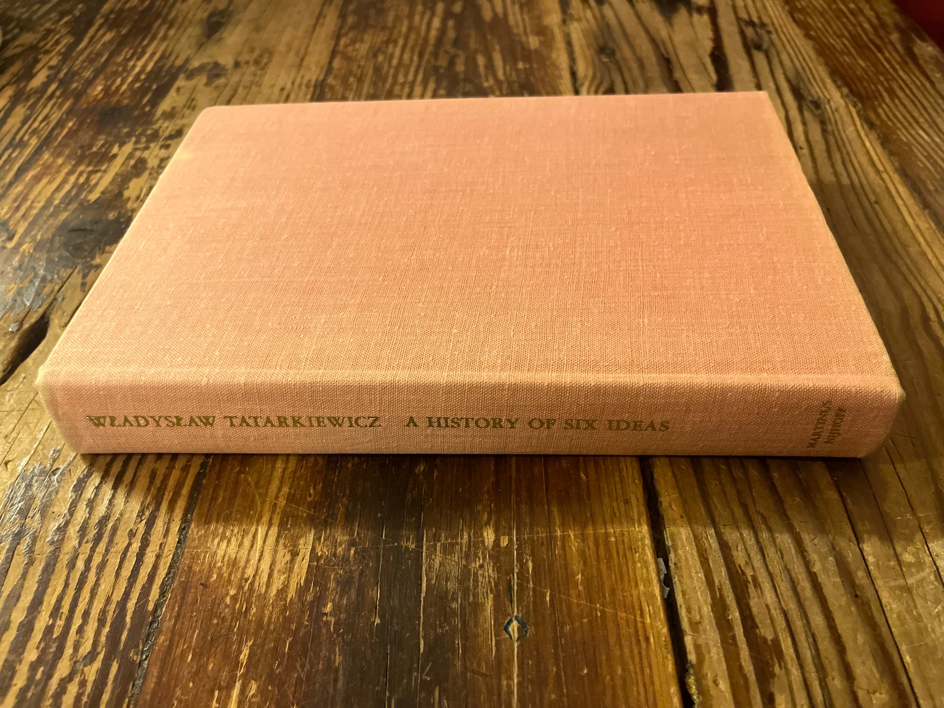 Pink book titled 'A History of Six Ideas' by Wladyslaw Tatarkiewicz on a wooden surface