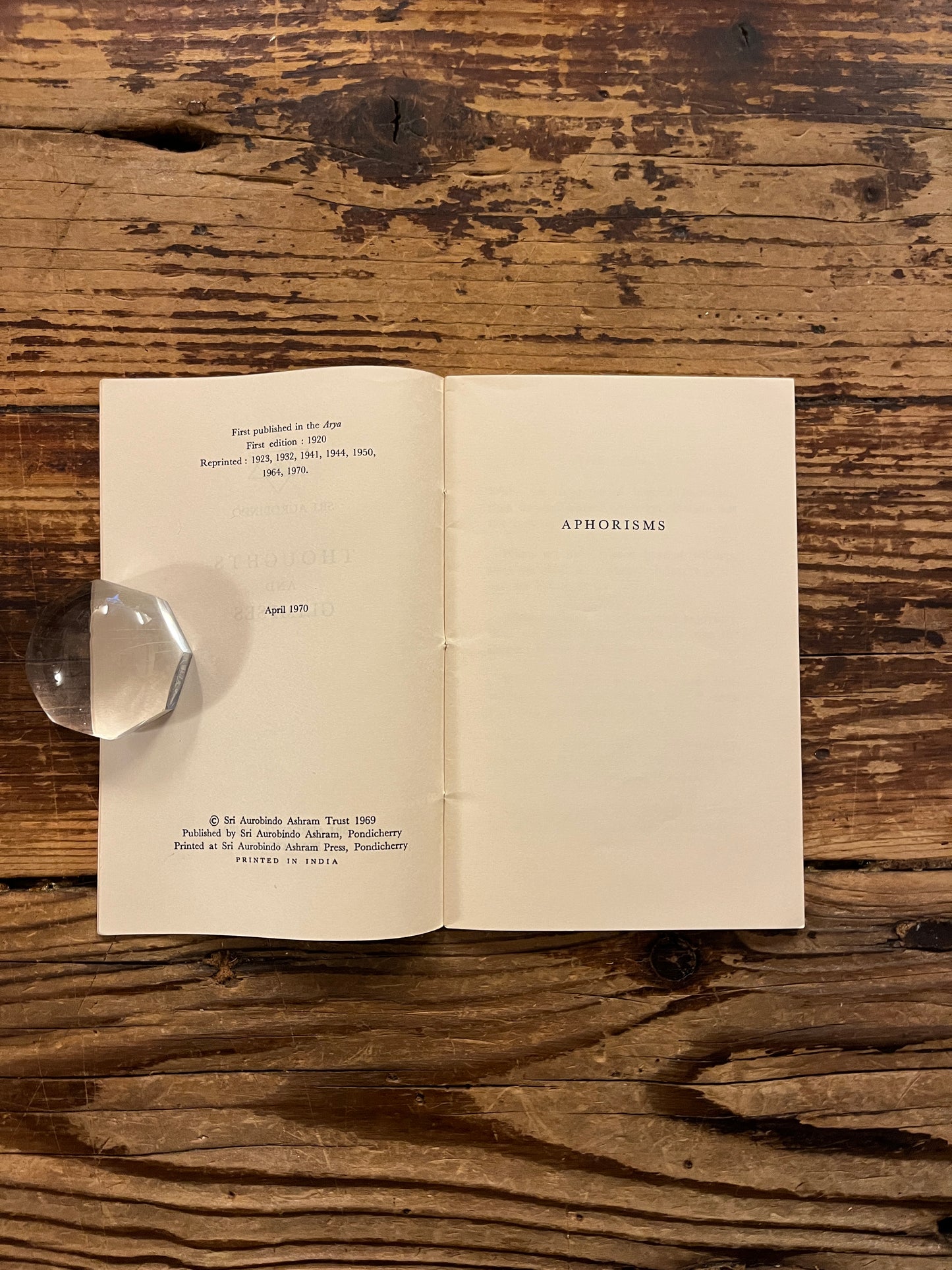 Open booklet titled 'Thoughts and Glimpses' by Sri Aurobindo on a wooden surface