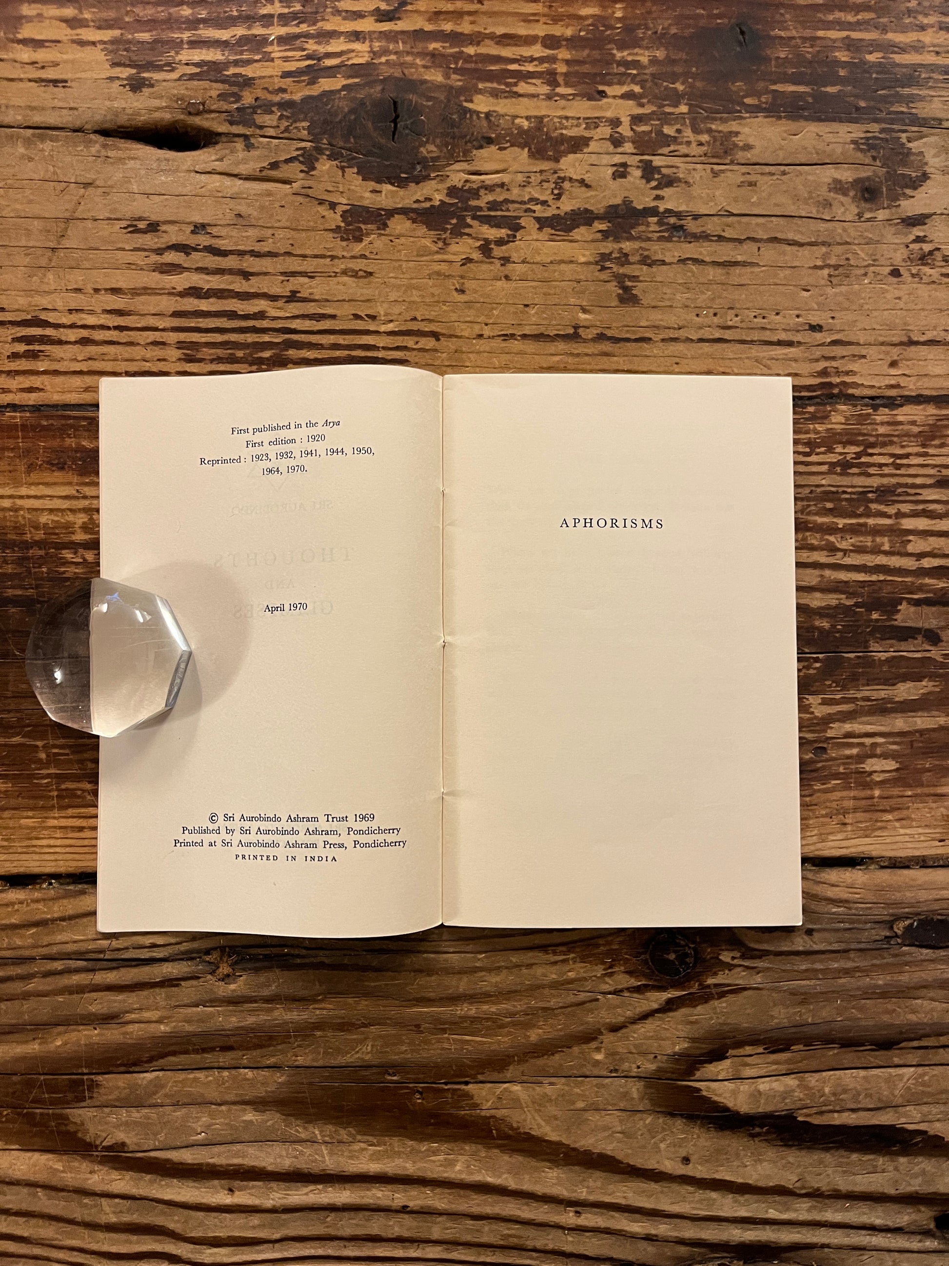Open booklet titled 'Thoughts and Glimpses' by Sri Aurobindo on a wooden surface