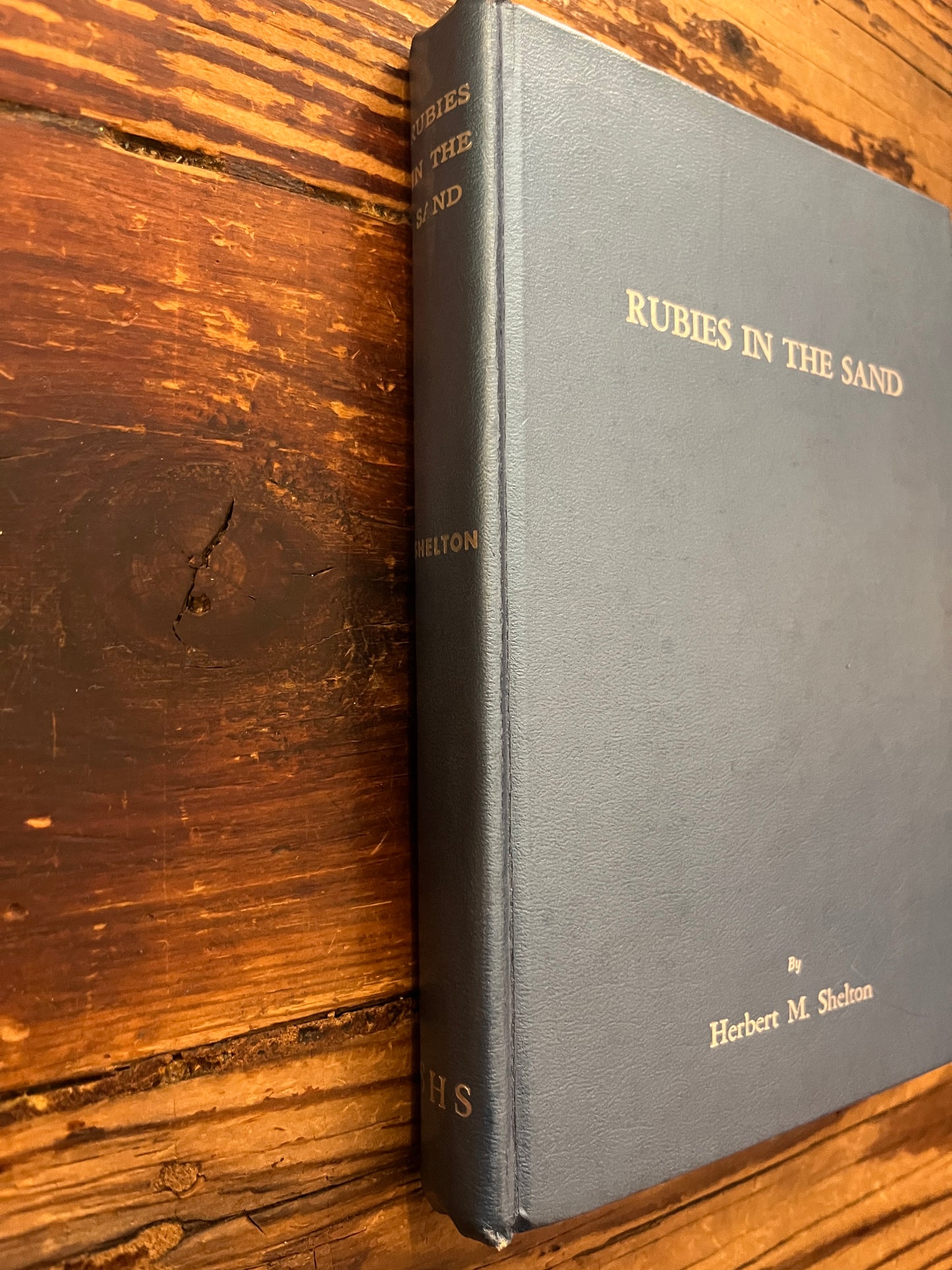 Spine of book titled 'Rubies in the Sand' by Herbert M. Shelton on a wooden surface