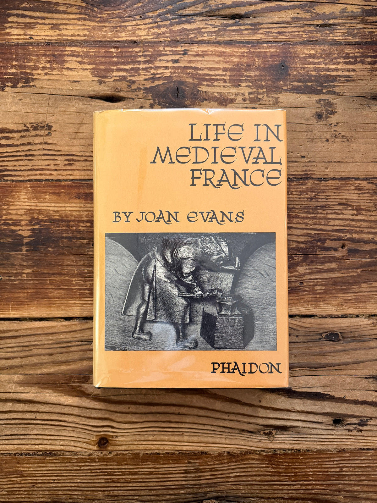 The front cover of a book titled 'Life in Medieval France' by Joan Evans, on a wooden surface