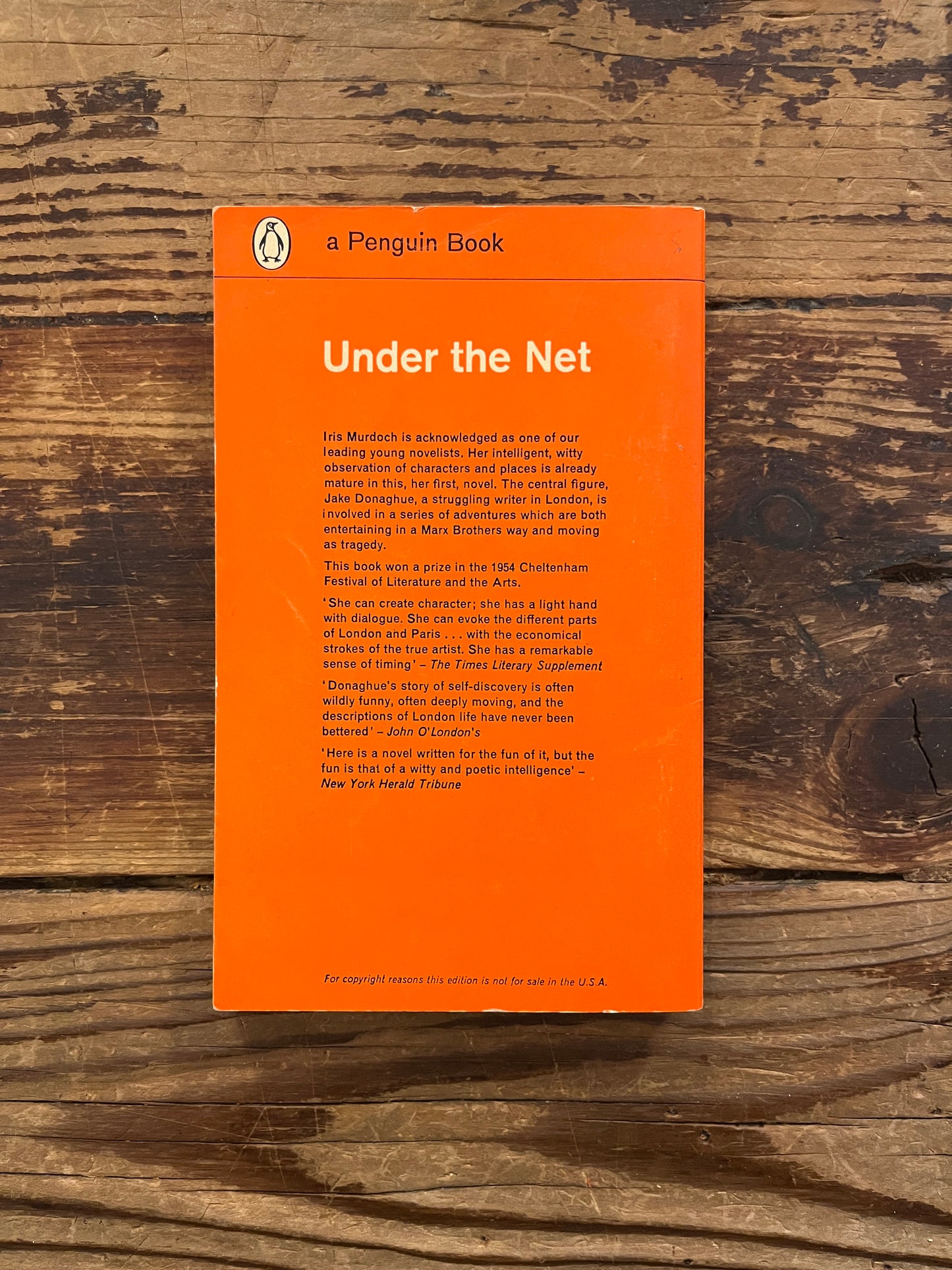 Back cover of Penguin book titled 'under the Net' by Iris Murdoch on a wooden surface