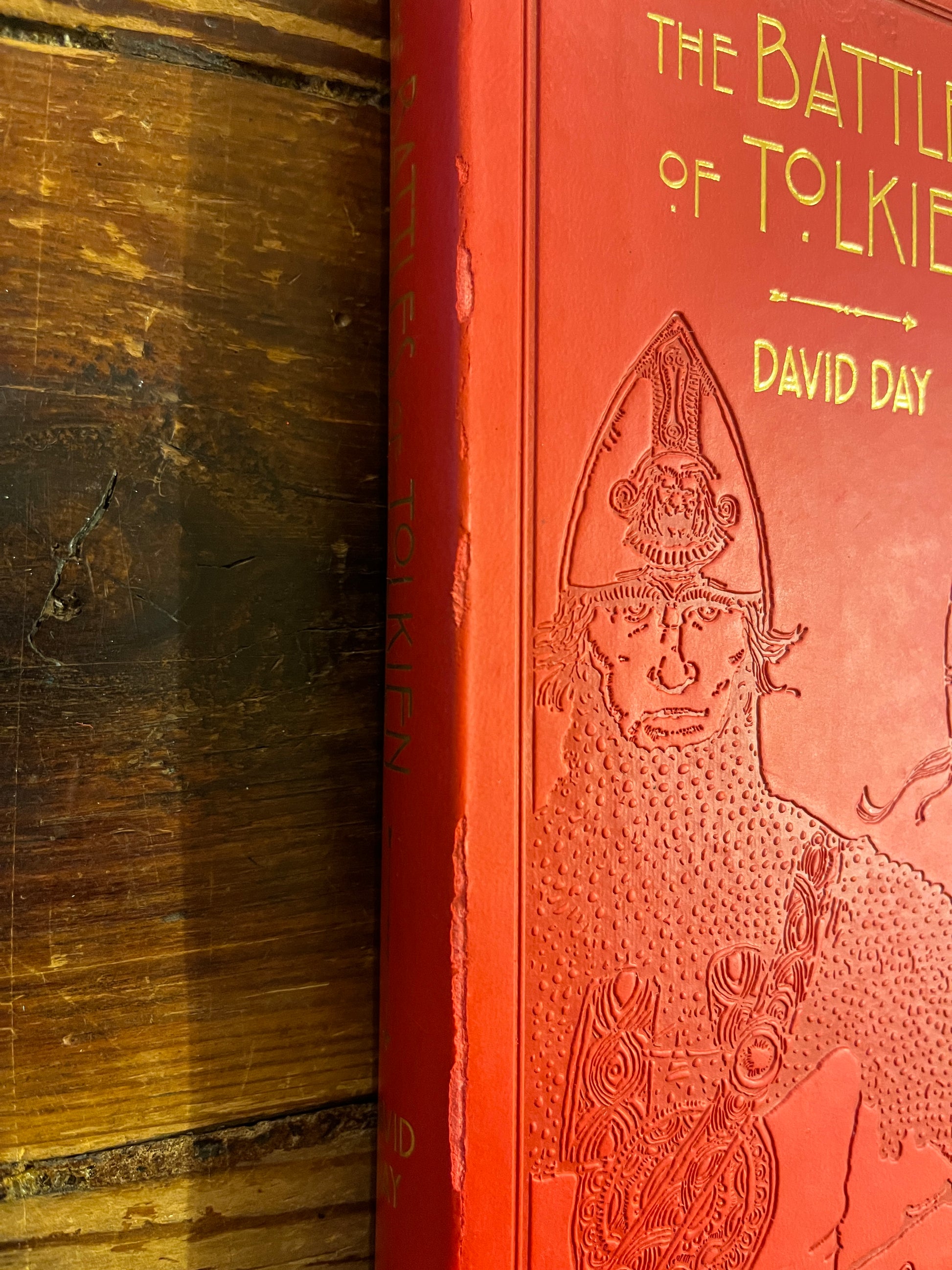 Spine showing very light wear and tear of book titled 'The Battles of Tolkien' by David Day on a wooden surface 