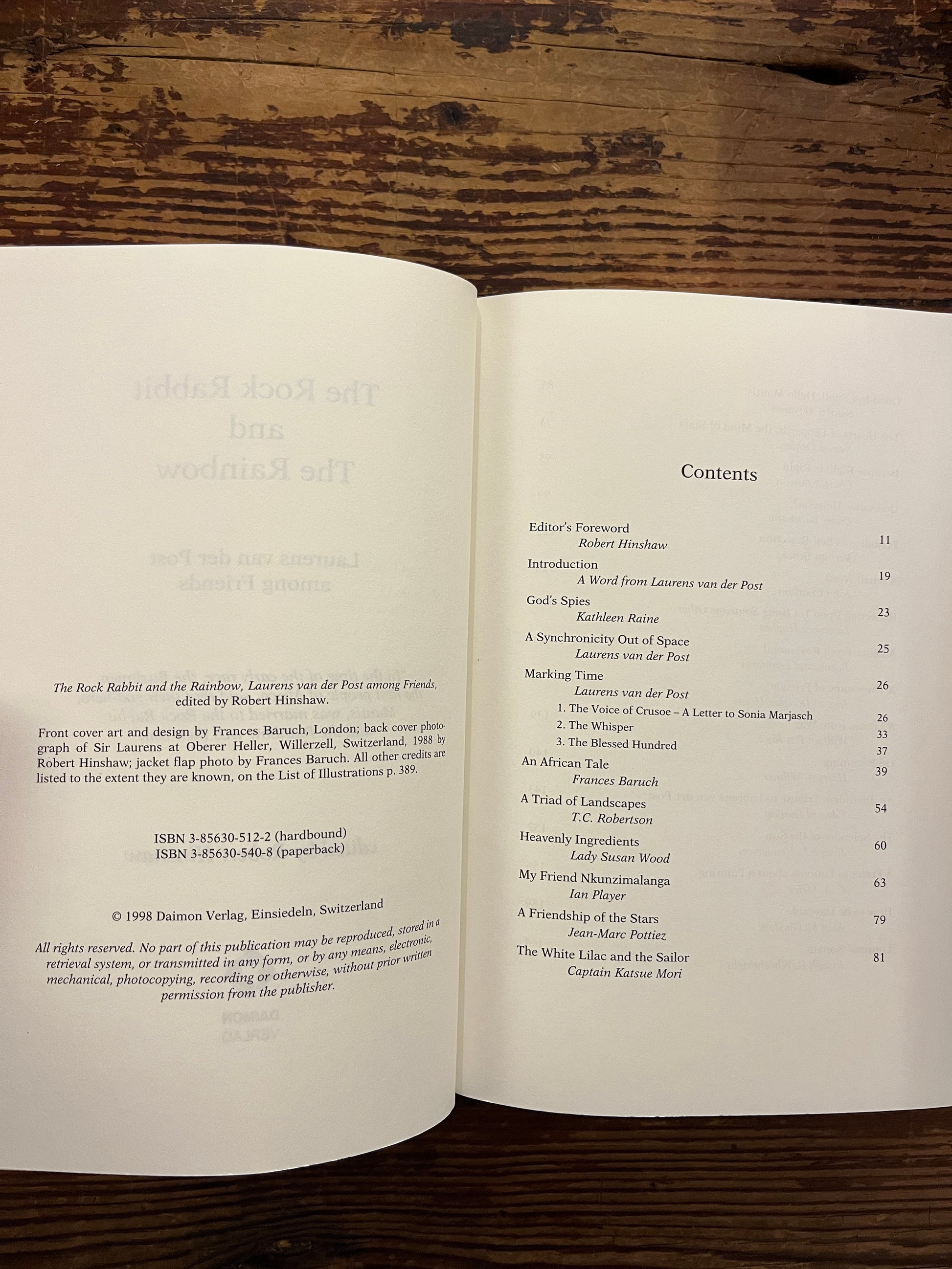 Open book showing the contents, book with the title 'The Rock Rabbit and The Rainbow' by Laurens van der Post on a wooden surface