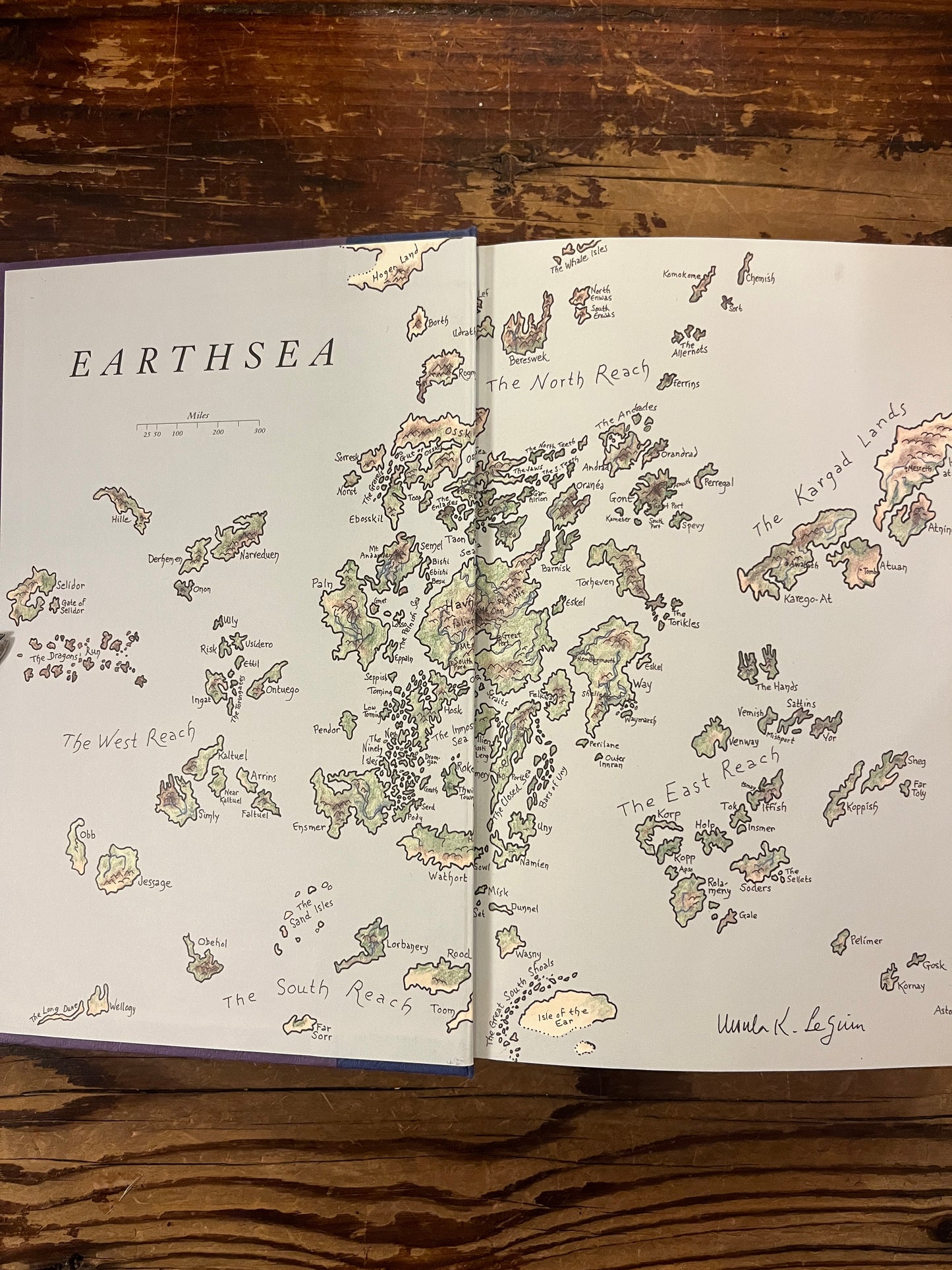 Open book showing the map of Earthsea from the book titled 'Tales from Earthsea' by Ursula K. Le Guin on wooden background