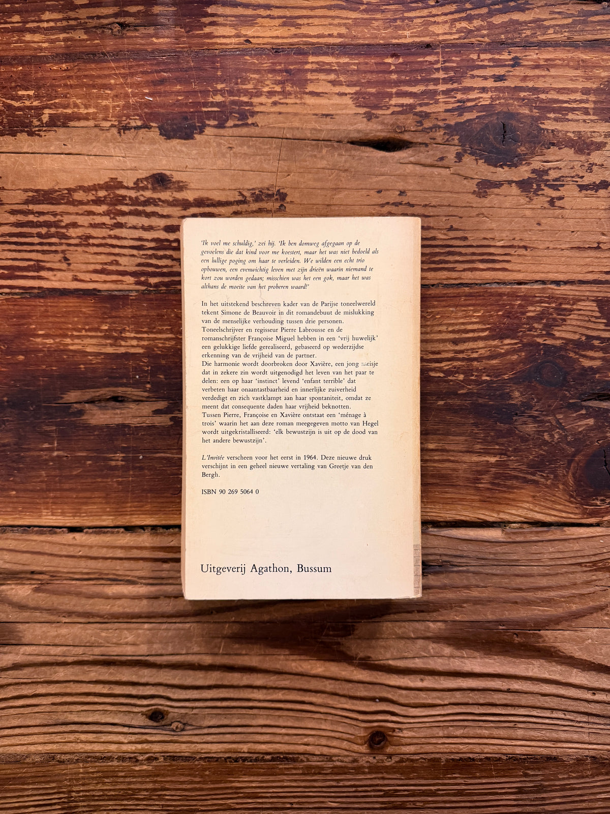 Achterkant van boek met de titel 'Uitgenodigd, l'invitée' door Simone de Beauvoir op een houten achtergrond