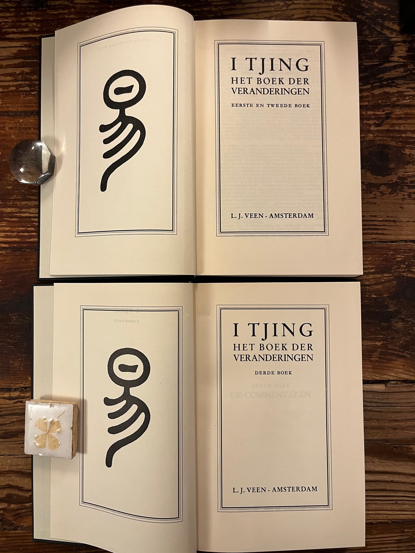 Twee open boeken met de titel 'I Tjing: Het Boek Der Veranderingen' op een houten achtergrond